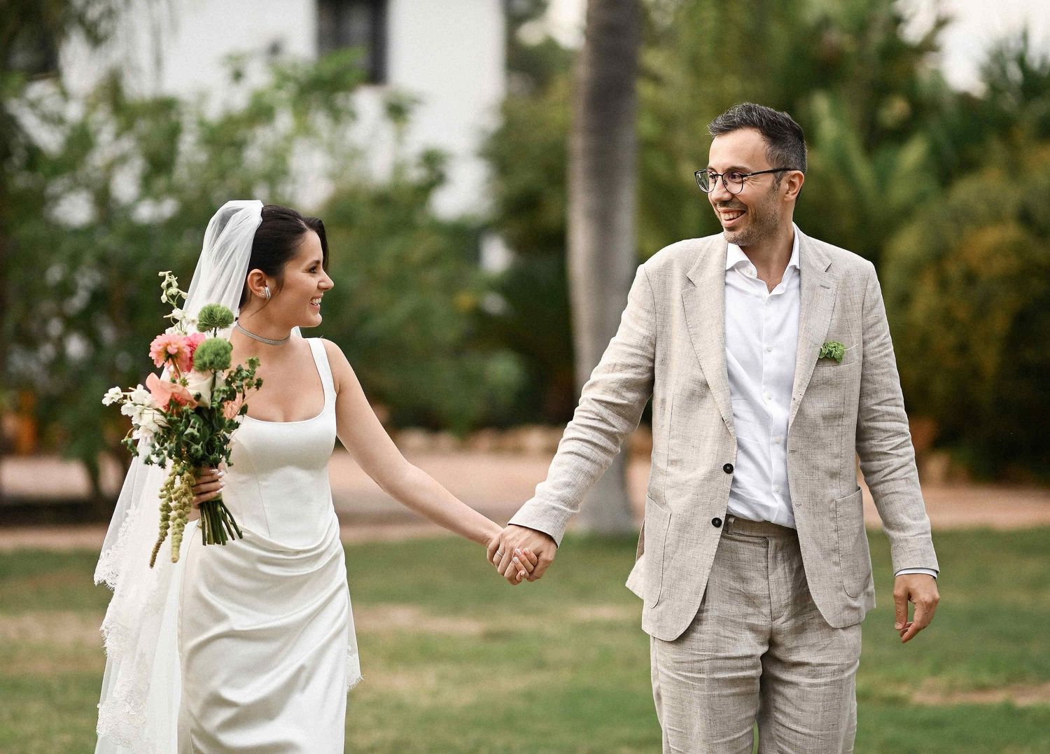 Semih and Maya walking hand-in-hand through the lush greenery of Villa Paula, looking at each other with genuine smiles