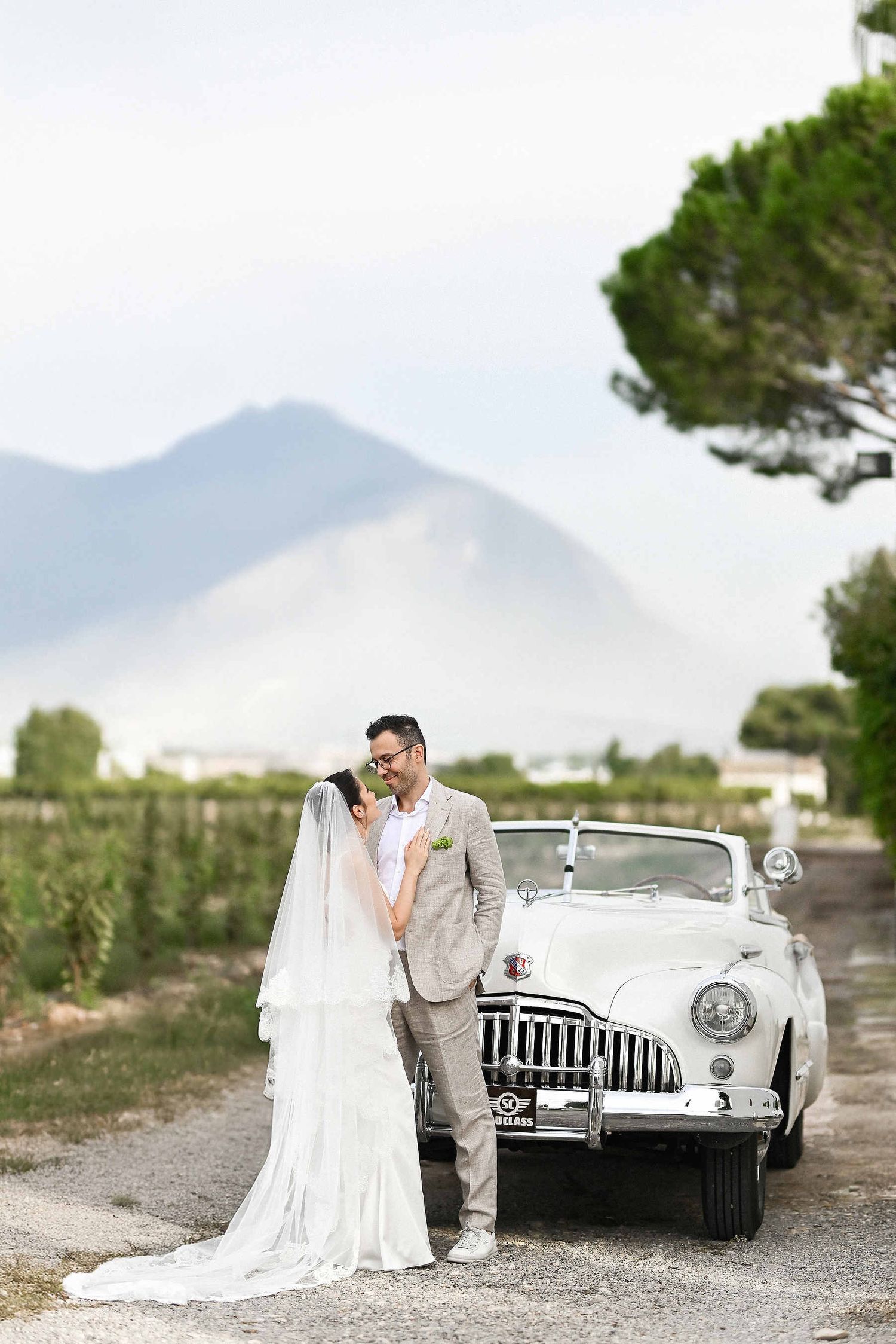 Destination wedding in Spain. A couple posing with a vintage retro car against a breathtaking mountain landscape backdrop