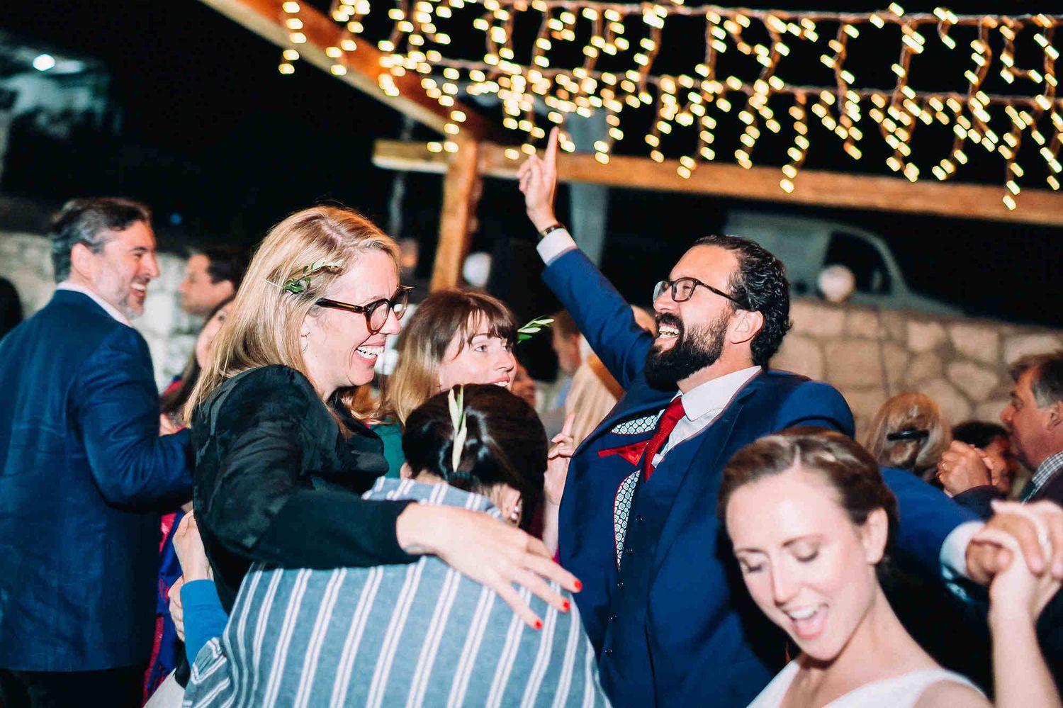 Bride and groom dancing with guests on a Milos island wedding dance floor. Dynamic energy at a Greek destination celebration.