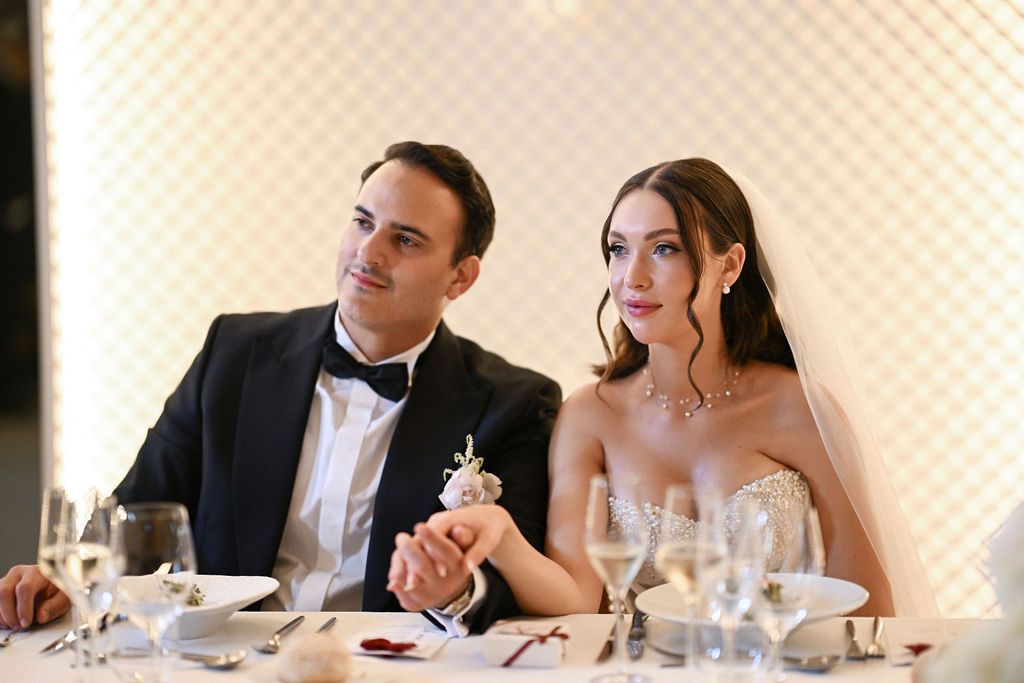 The newlyweds holding hands at their central head table during the wedding dinner inside the historic hall of Finca del Canónigo villa.
