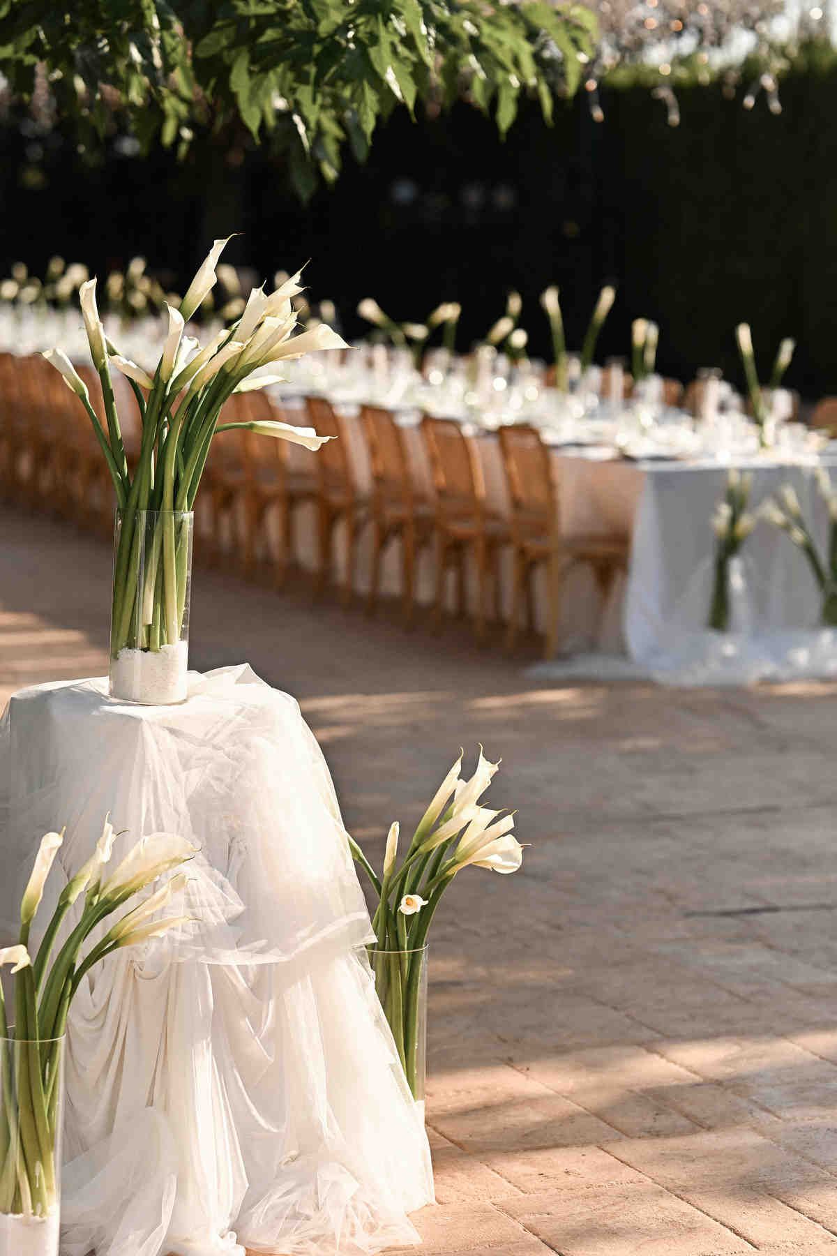 Minimalist wedding floral design featuring white calla lilies in glass vases on a tulle-covered stand at Alquería Kukala.