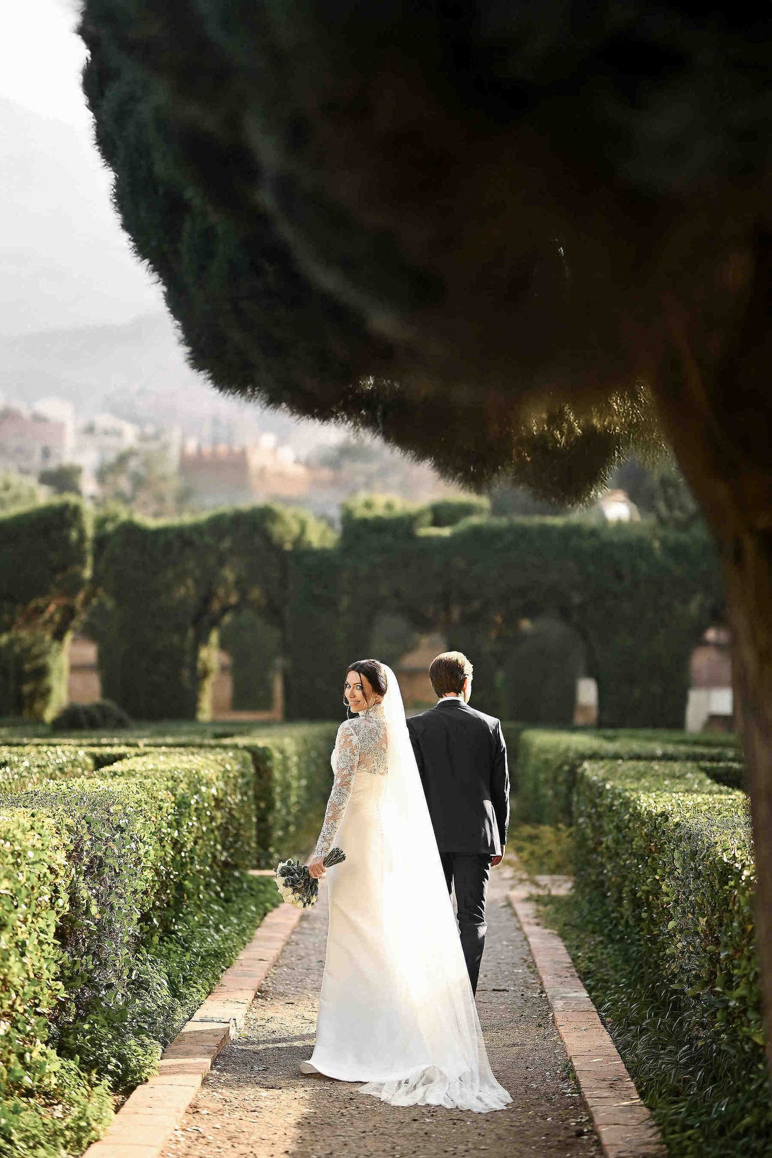 Wedding photography in Spain. A bride looking back while walking with the groom through a picturesque European park setting