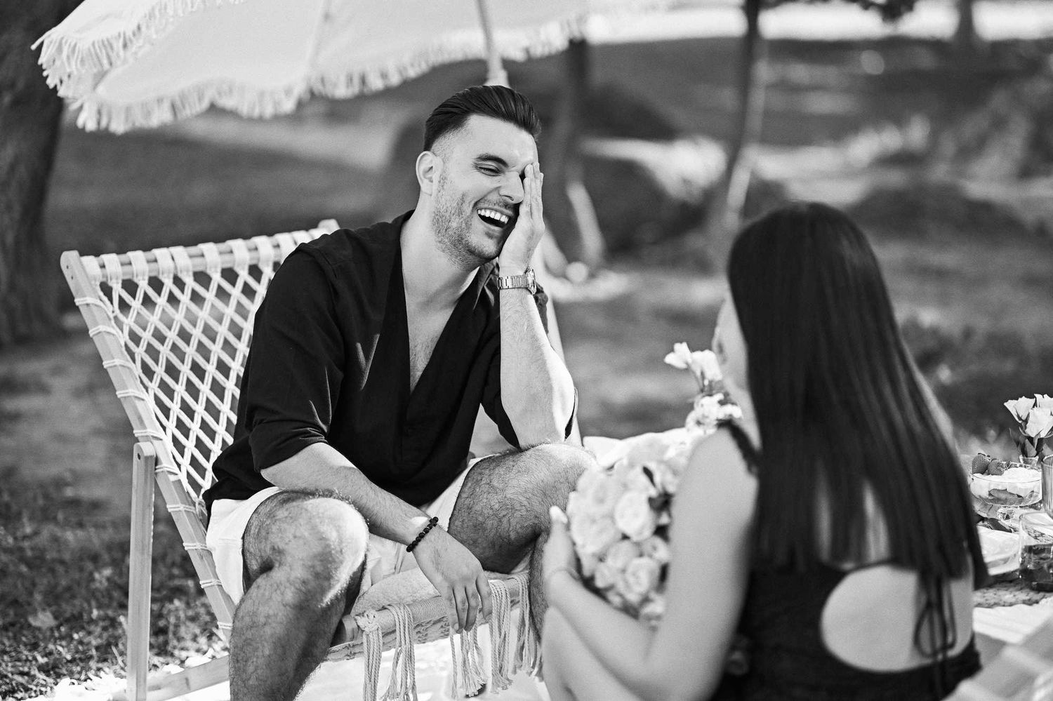 Black and white candid shot of the groom laughing with relief and joy right after his successful Jardin del Real proposal.