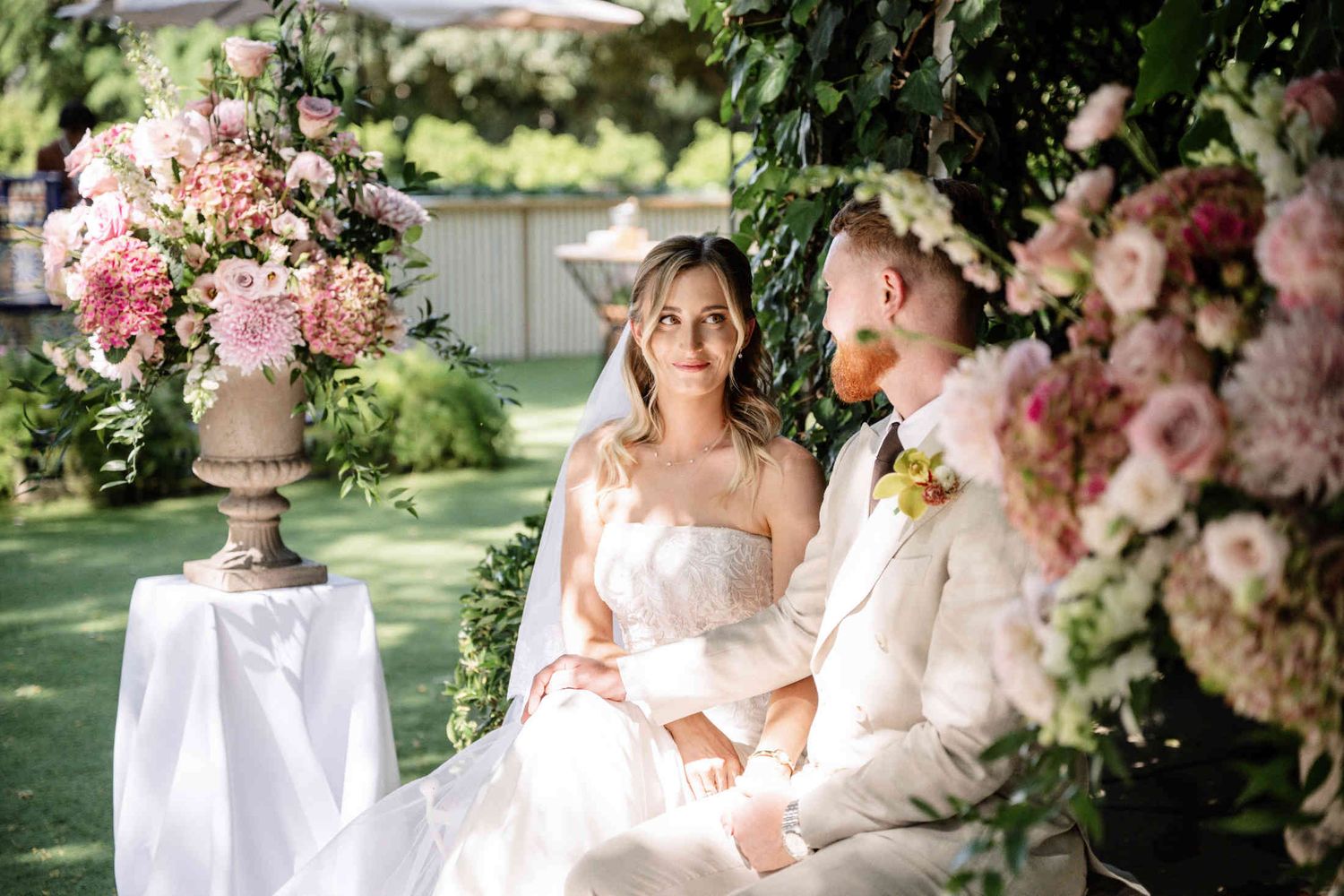 Happy bride and groom seated together during an elegant destination wedding ceremony in the lush gardens of Villa Dela, Valencia.