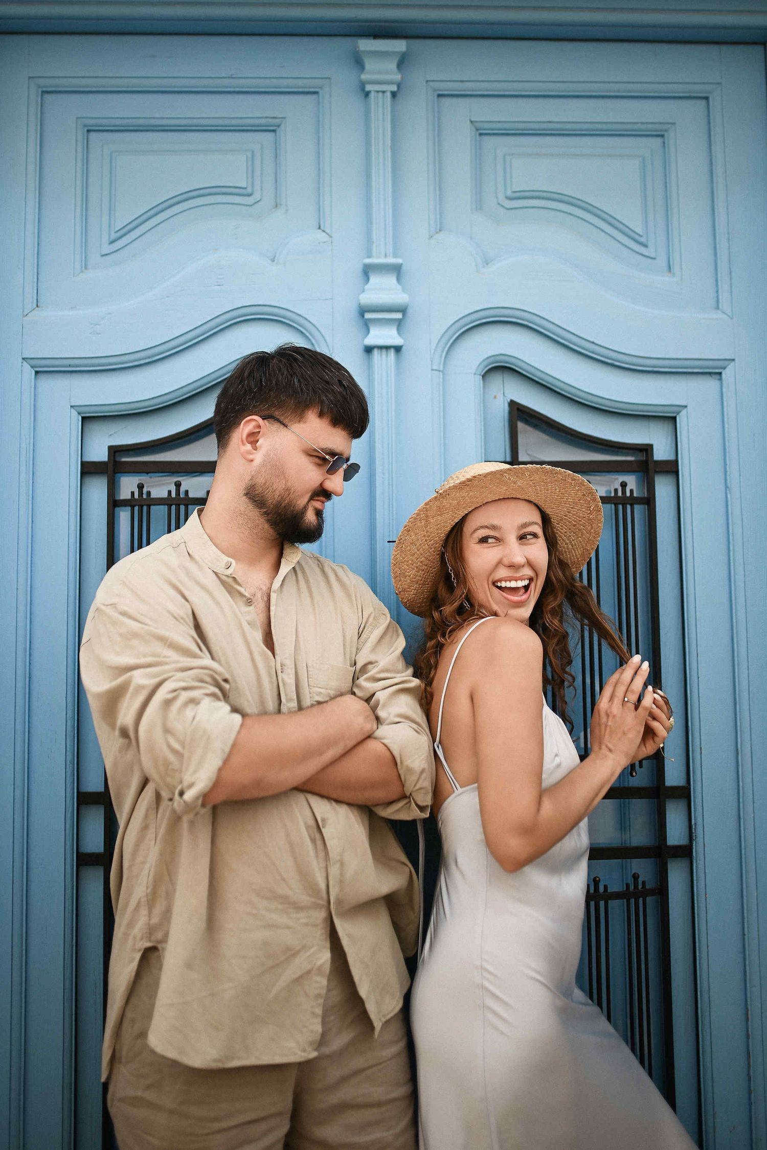 A joyful couple laughing in front of a traditional blue door in the white streets of Altea. Authentic engagement photography