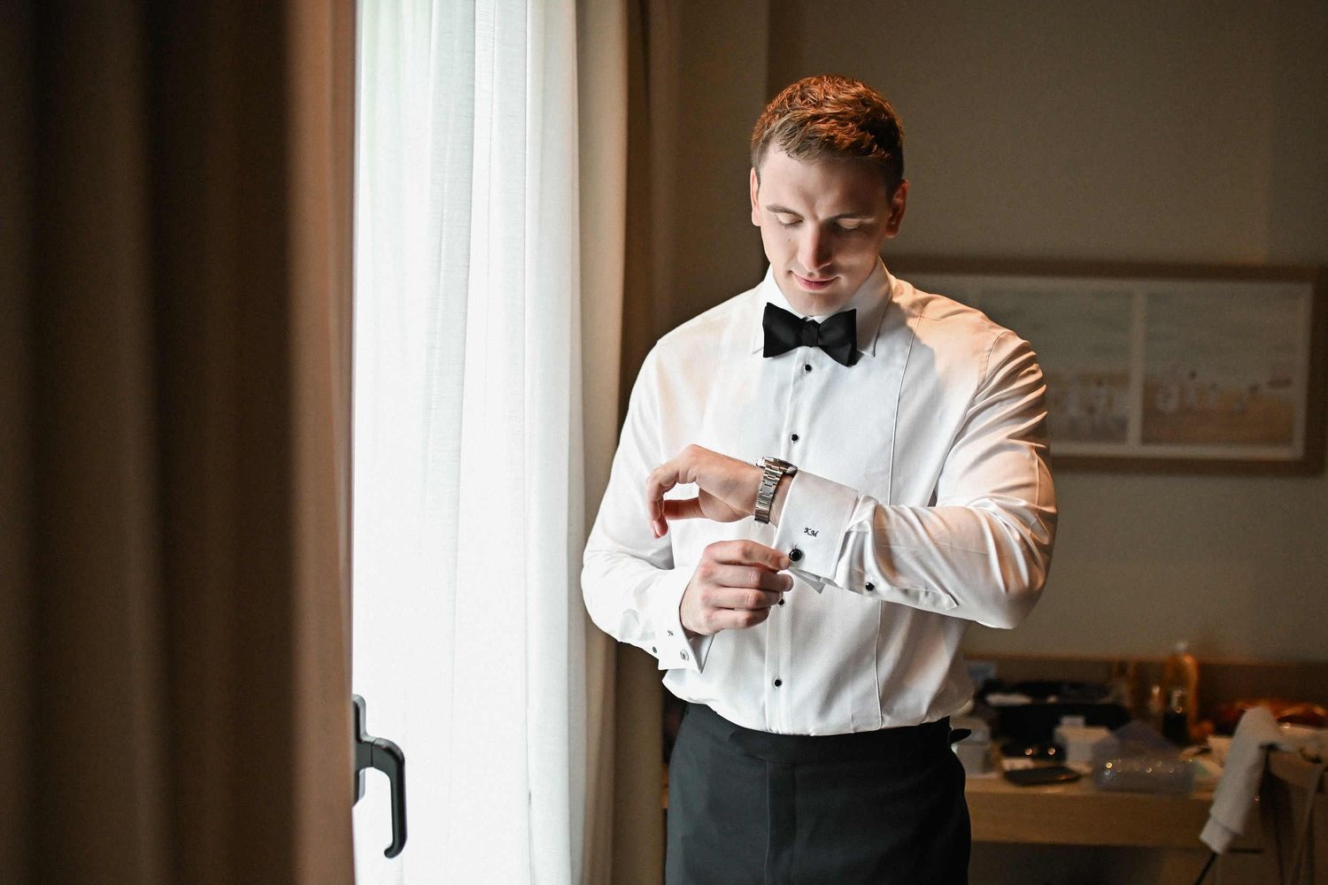 Groom adjusting his watch cufflinks near the window during wedding getting ready at Hotel Las Arenas Valencia