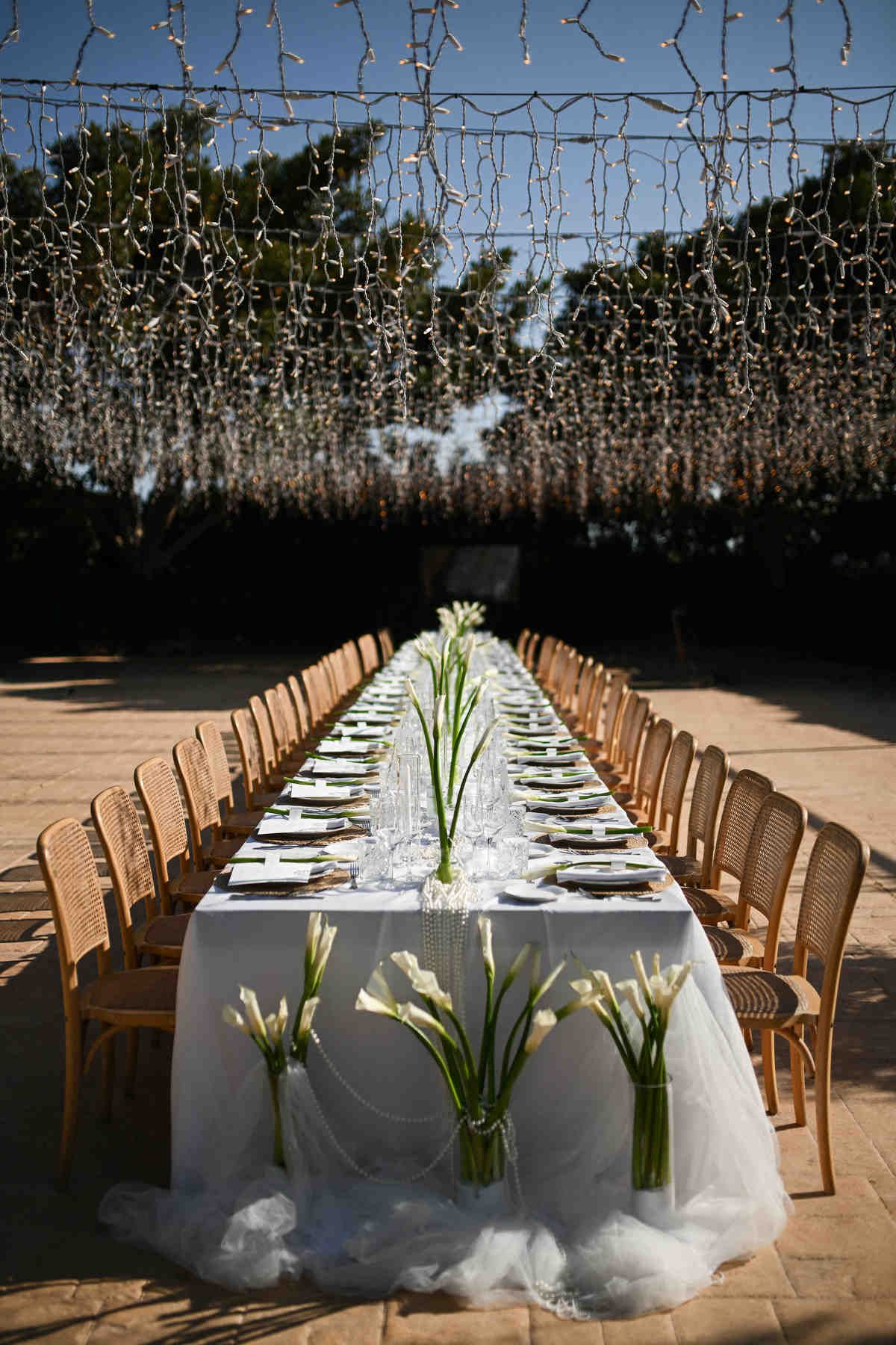 Symmetrical view of a long wedding reception table decorated with calla lily floral arrangements and fairy lights at Alquería Kukala.