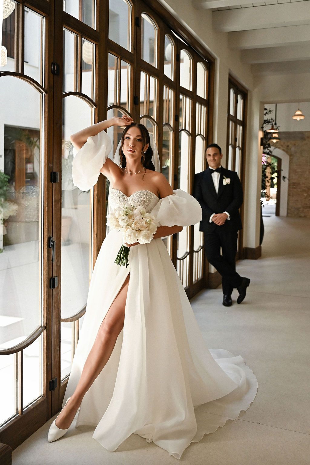 Full-length bridal portrait with the groom in the background, captured in the stained-glass window light inside Finca del Canónigo.