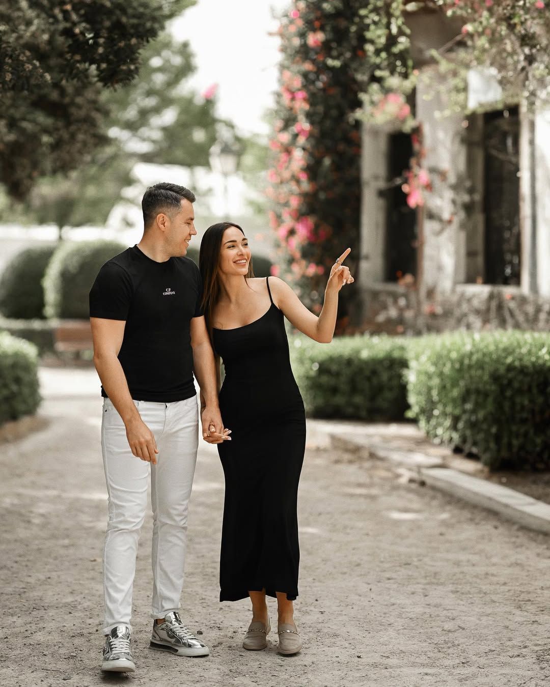A casual engagement photoshoot at Jardines del Real with a couple holding hands and walking along a sunlit gravel path.