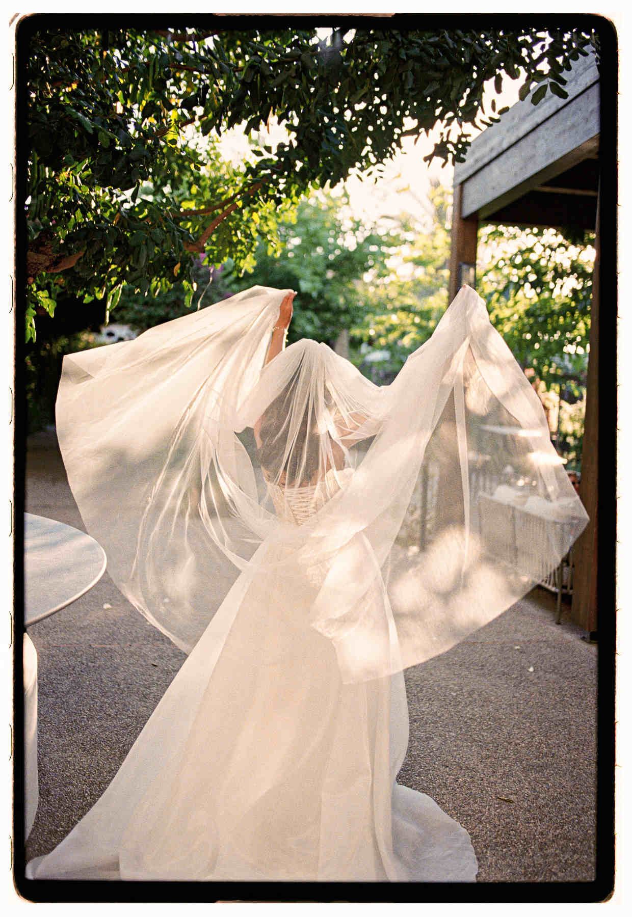 Atmospheric back view of a bride with a moving veil, captured on Nikon F5 and Kodak Portra film in Spain.