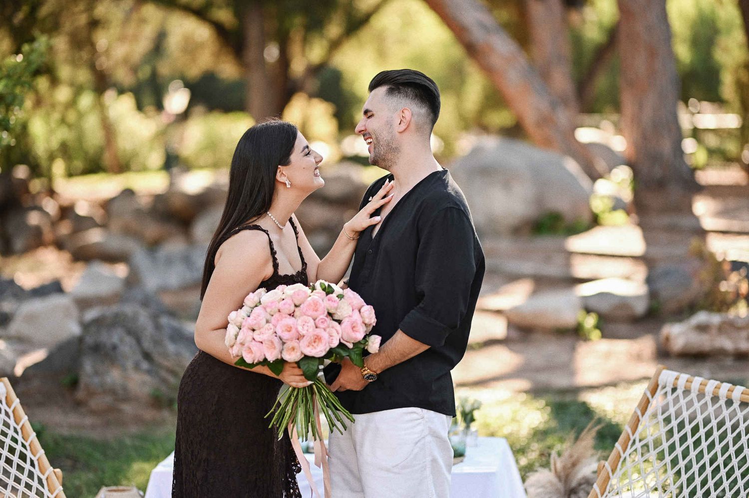 Newly engaged couple laughing together holding a pink rose bouquet after a surprise proposal in Valencia