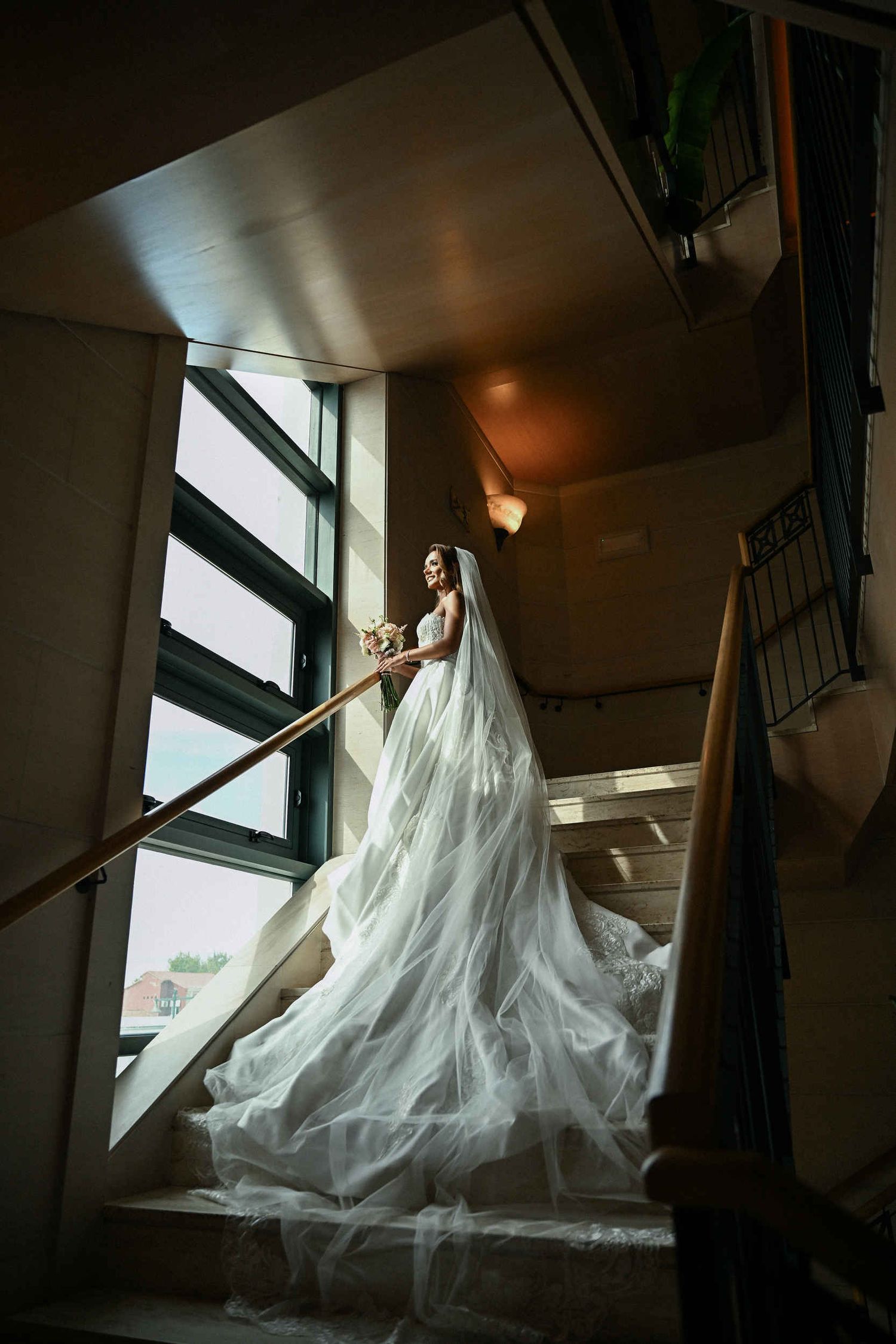 Bride in a beaded gown with a long flowing veil standing on a grand staircase at Hotel Las Arenas Valencia.