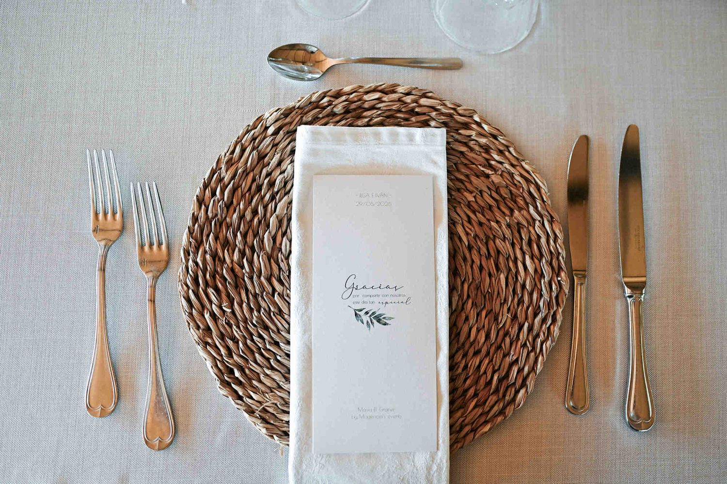 High angle view of a wedding table place setting with a round wicker placemat, silverware, and menu.