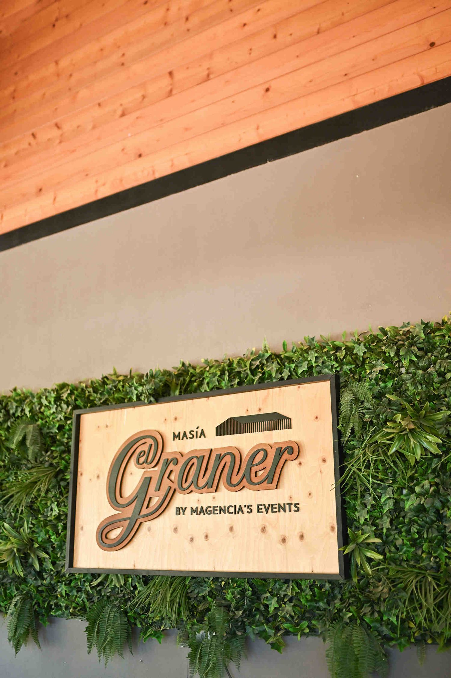 Close-up of the wooden Masia El Graner welcome sign decorated with green leaves at a Valencia wedding venue.