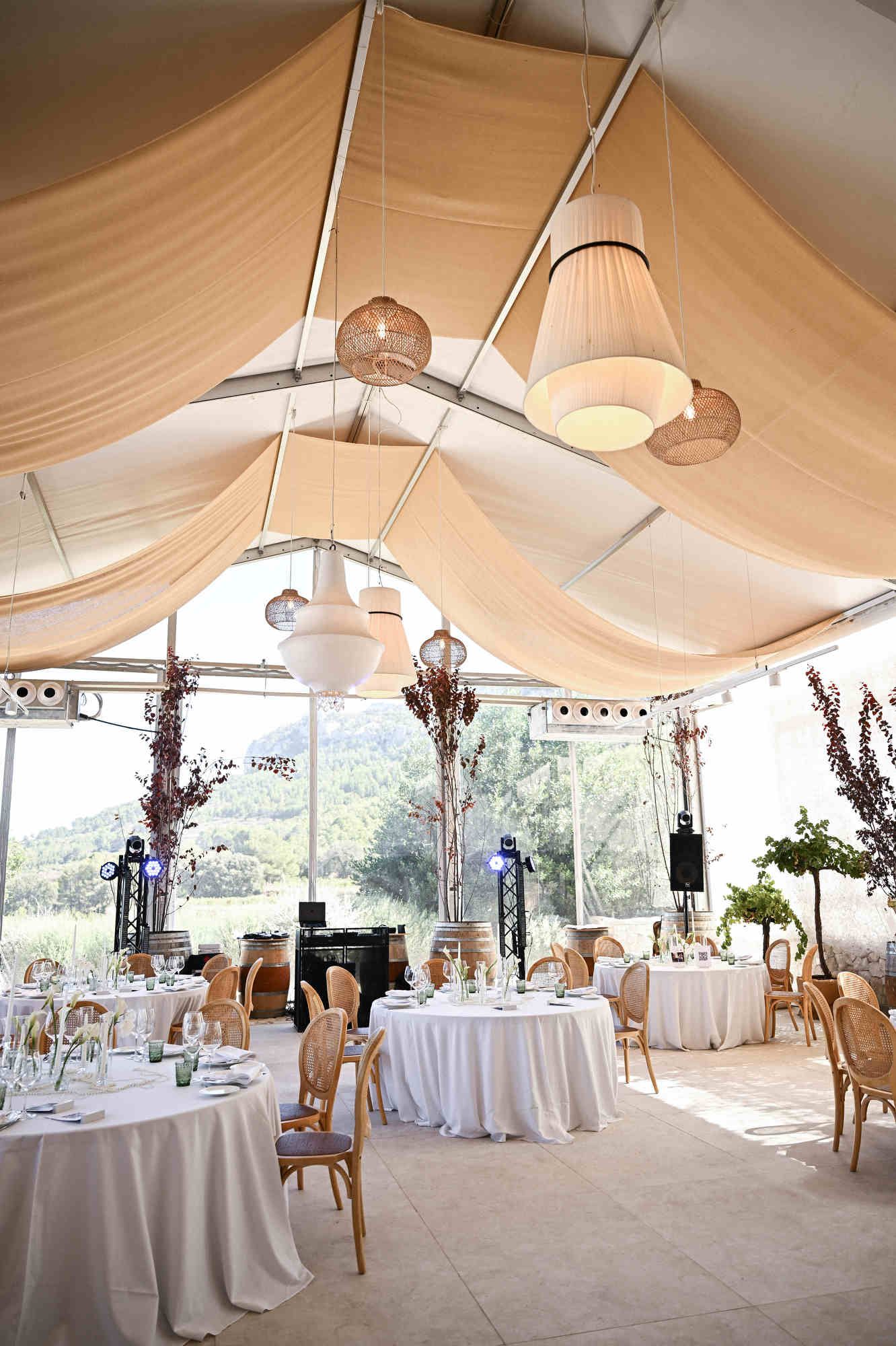 Beautiful wedding reception space featuring a draped ceiling, woven lamps, and a DJ setup in Alicante.