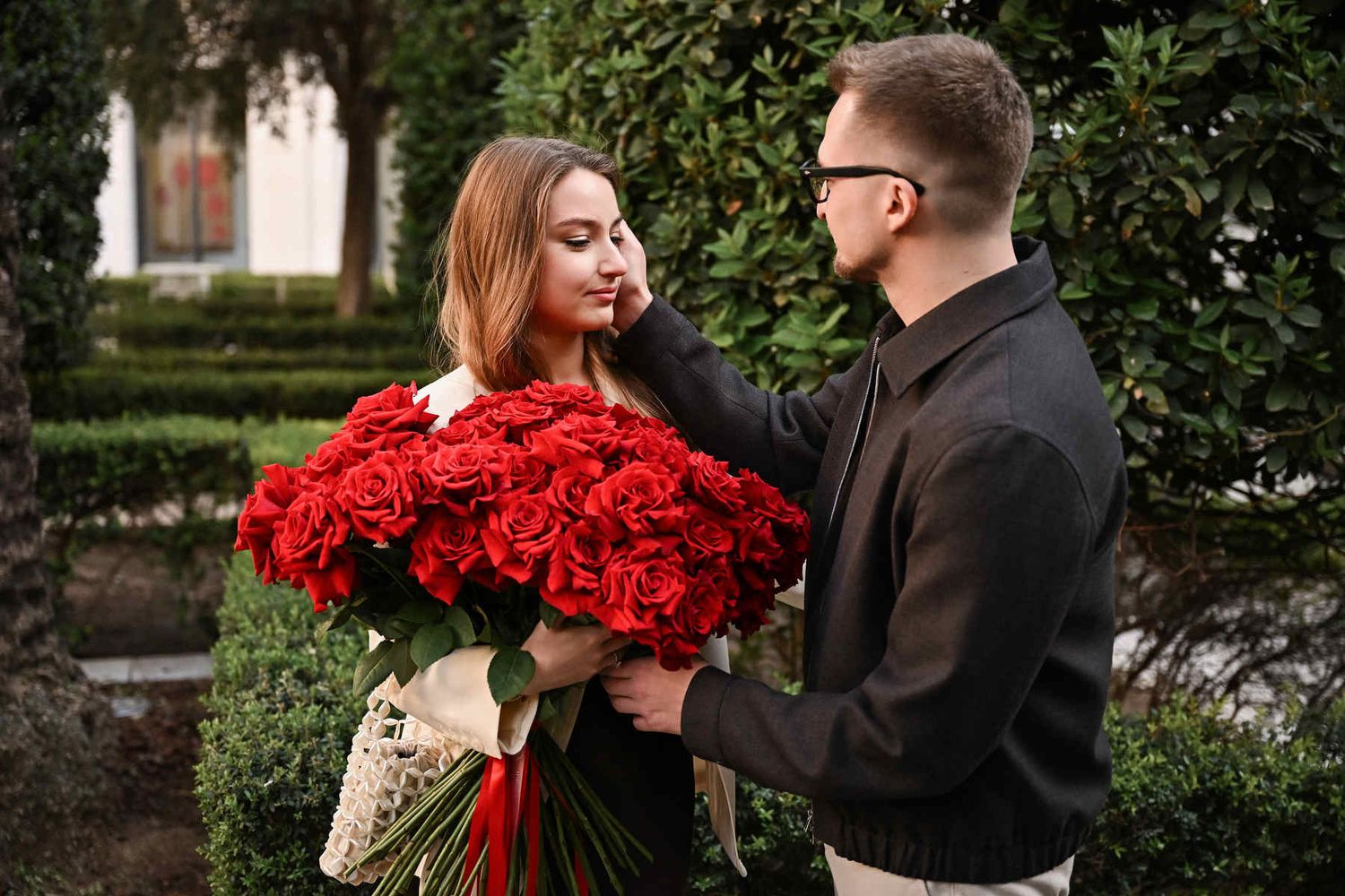 A groom-to-be gives his fiancée a massive bouquet of red roses after a successful surprise proposal.