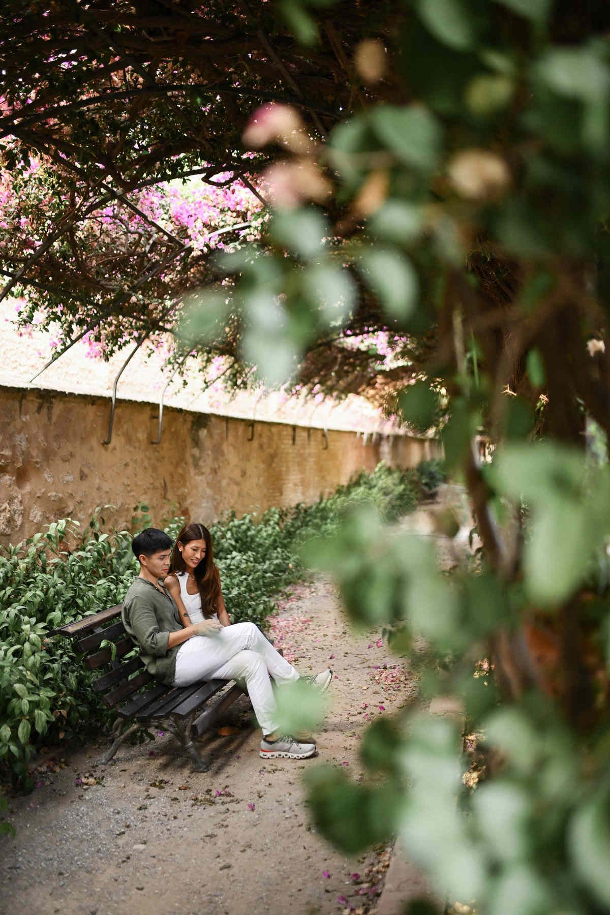 A couple relaxing on a bench under a beautiful floral tunnel during their Valencia engagement shoot.