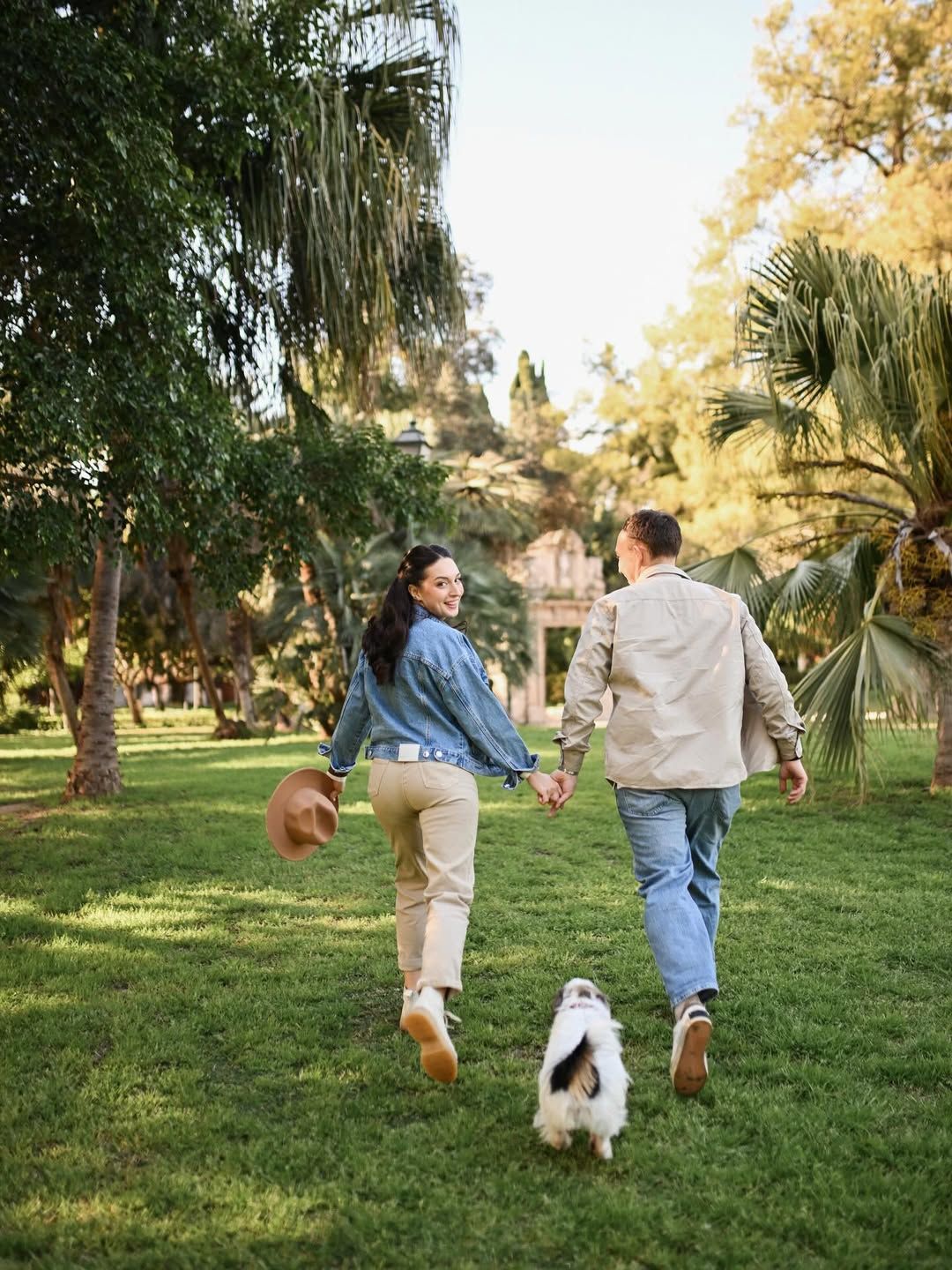 Couple walking with their dog through the green paths of Turia Gardens during a relaxed engagement photoshoot in Valencia.