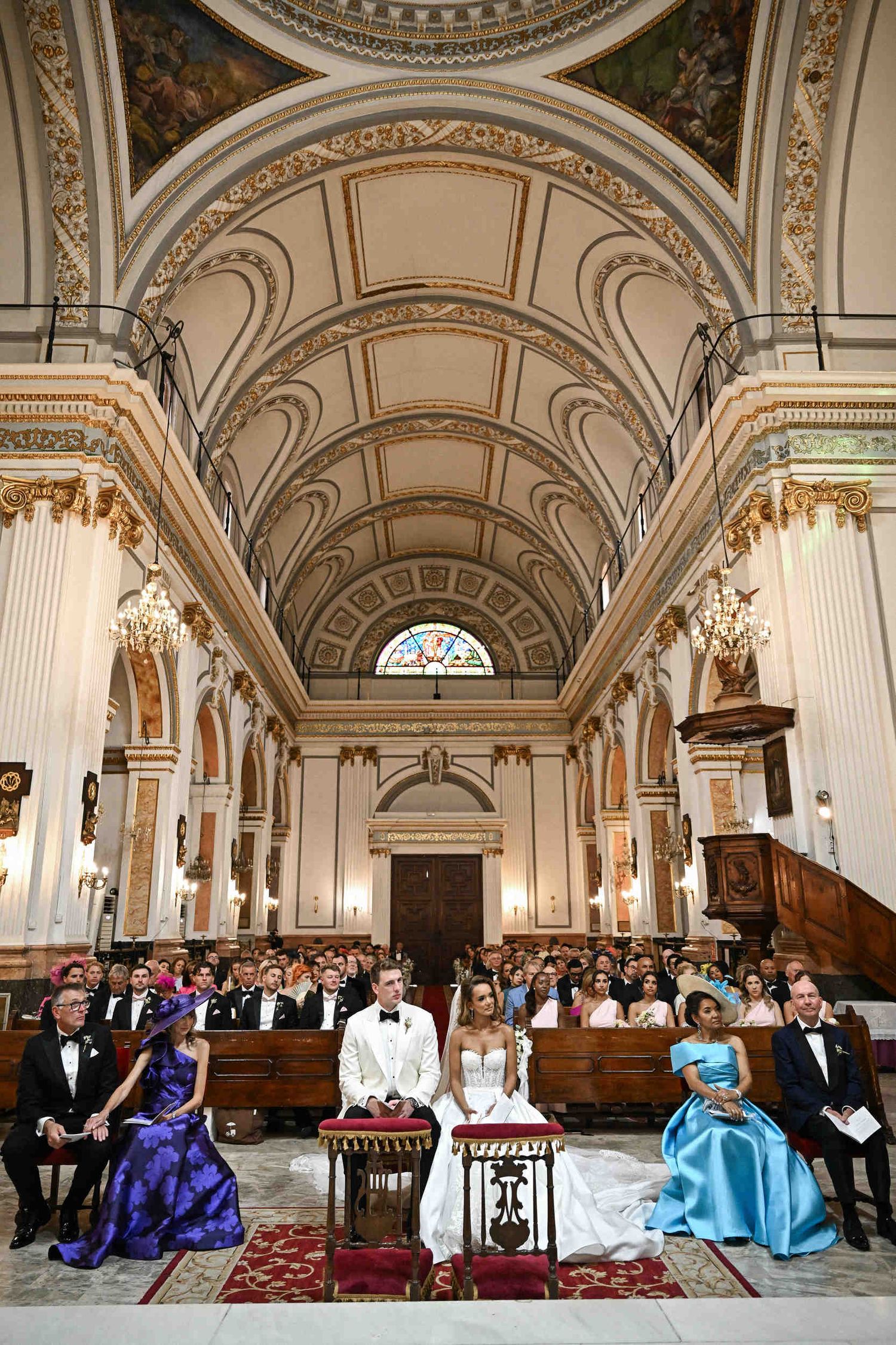 Bride and groom sitting before the altar during a Catholic wedding ceremony inside a grand Valencia church