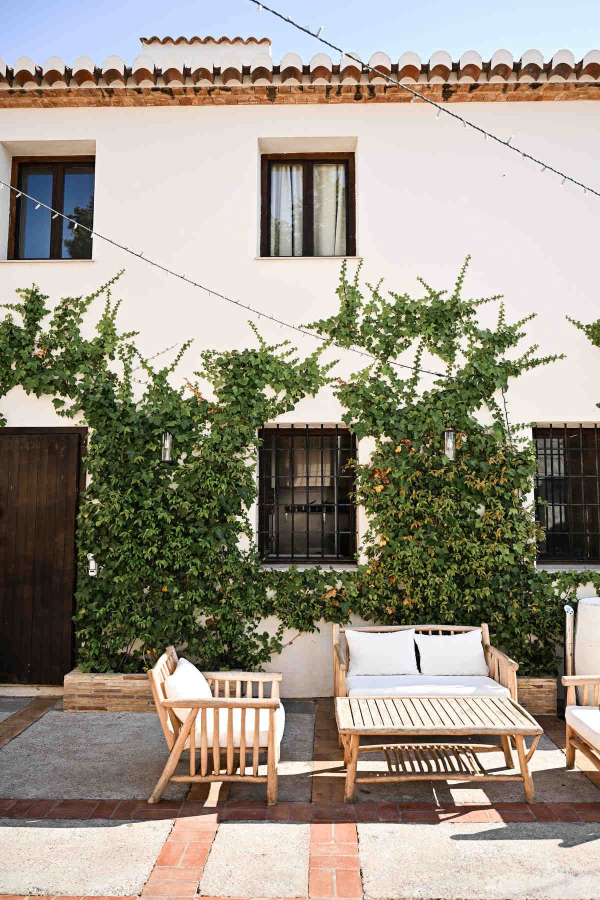 Bright white wall of the finca building covered in lush ivy with wooden outdoor lounge chairs.