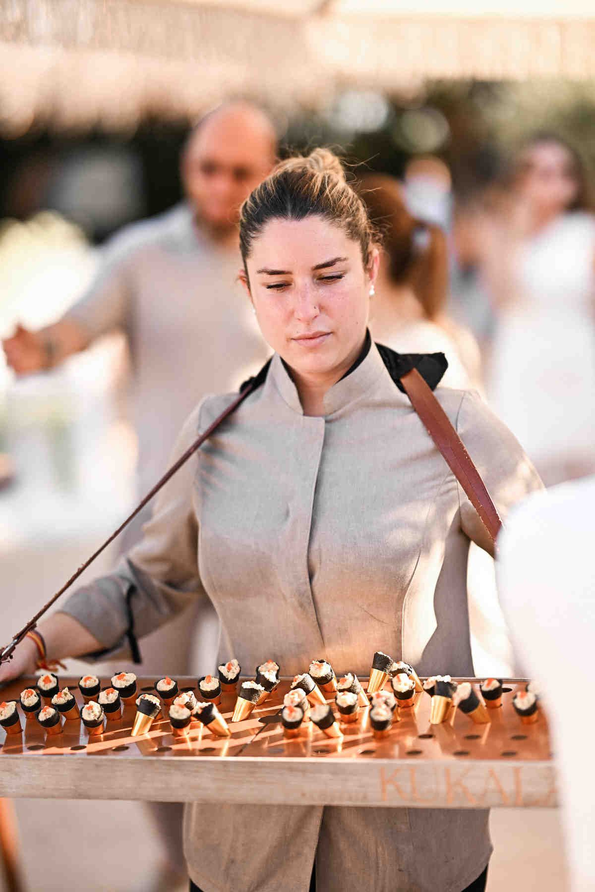 A waitress serving elegant cone appetizers during an outdoor wedding cocktail hour.