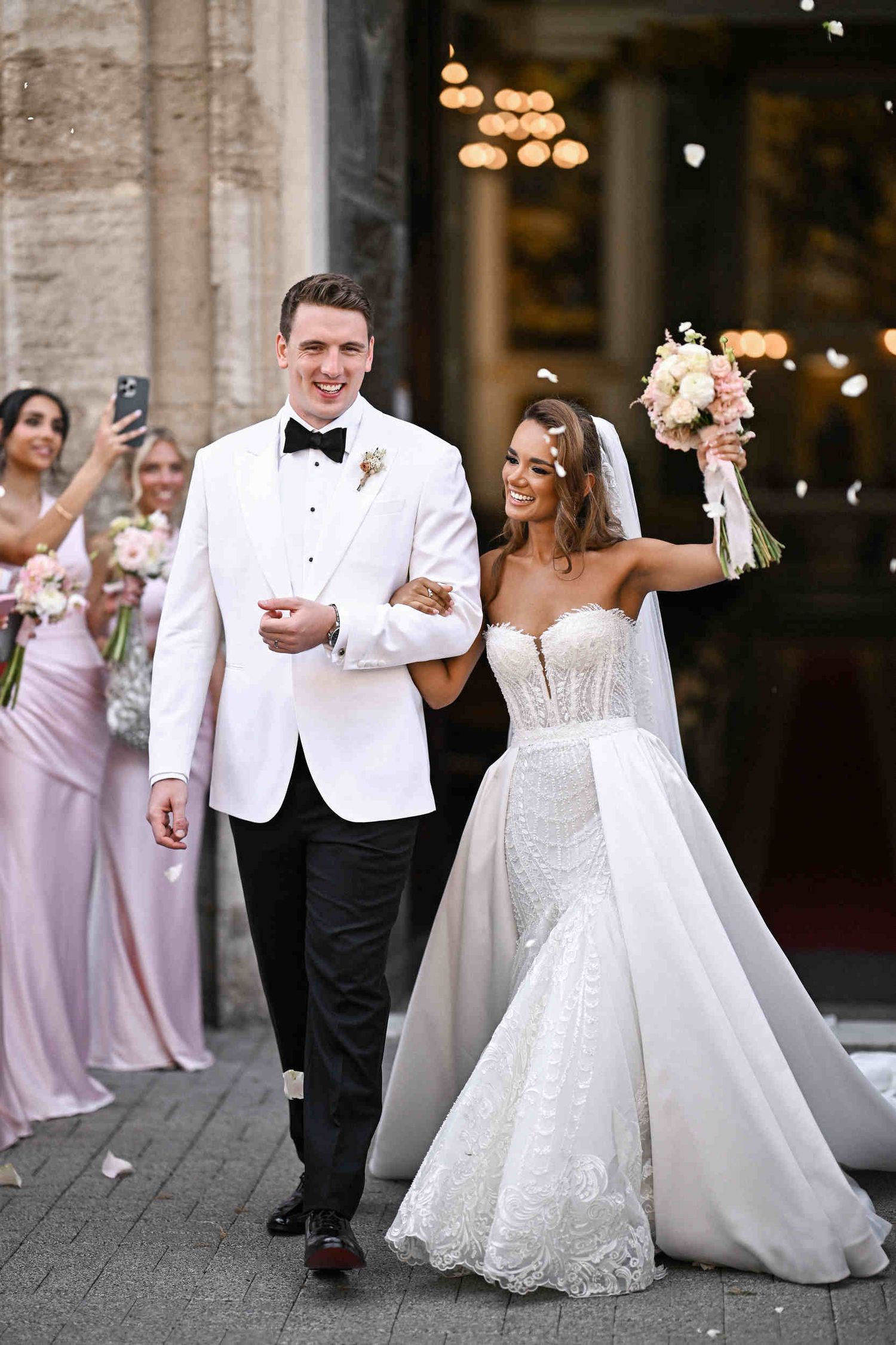 Newlyweds smiling and walking out of Parroquia de Santa Maria del Mar as guests toss flower petals