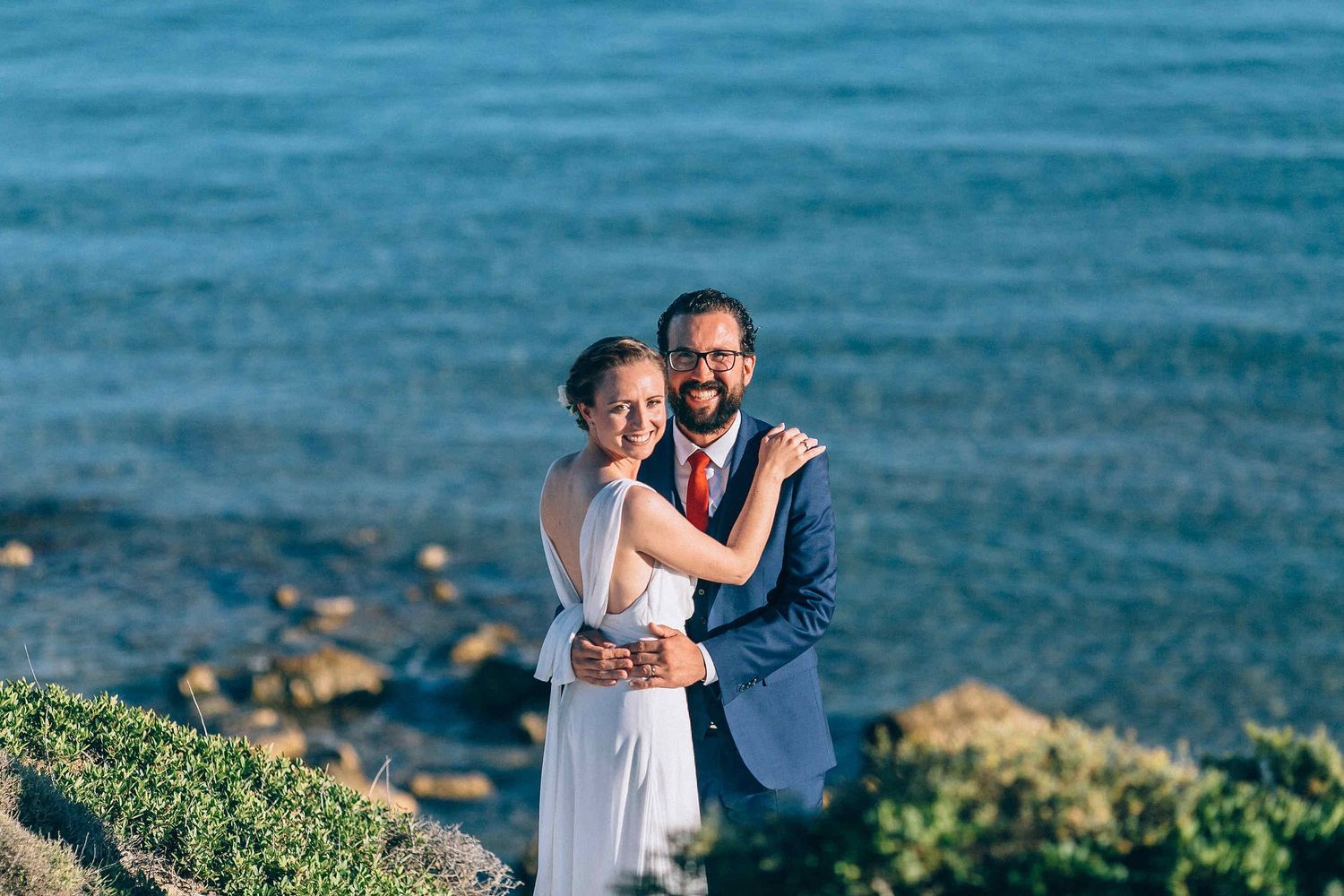 Minimalist composition of a couple standing before the vast Aegean sea horizon.