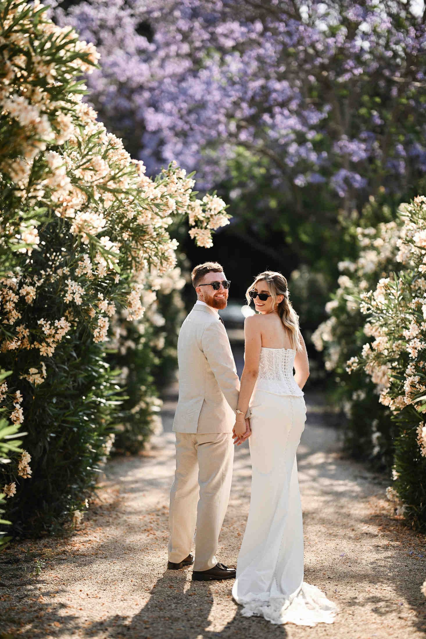 Full-length portrait of a couple in lush blooming Mediterranean gardens of Villa Dela, showing the long wedding dress train.