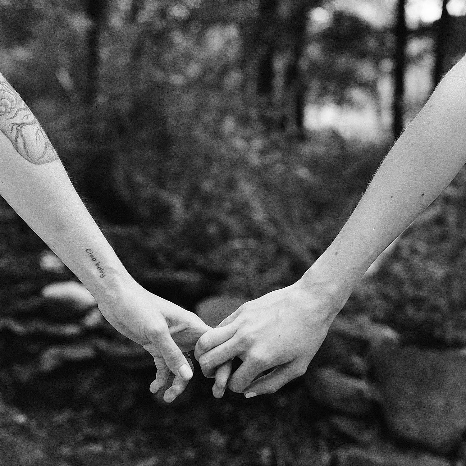Close-up black and white photo of hands with tattoos holding each other tenderly.