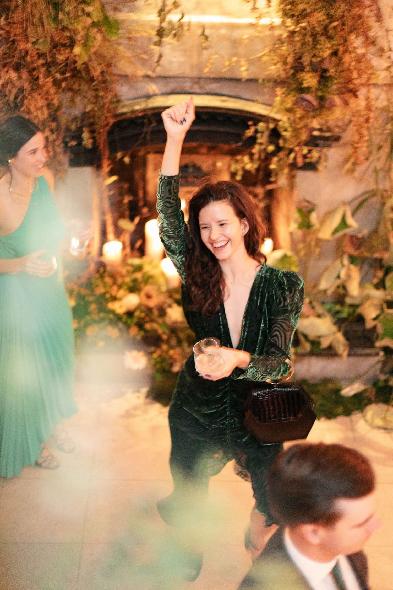People dancing and celebrating at an indoor wedding reception with decorative foliage.