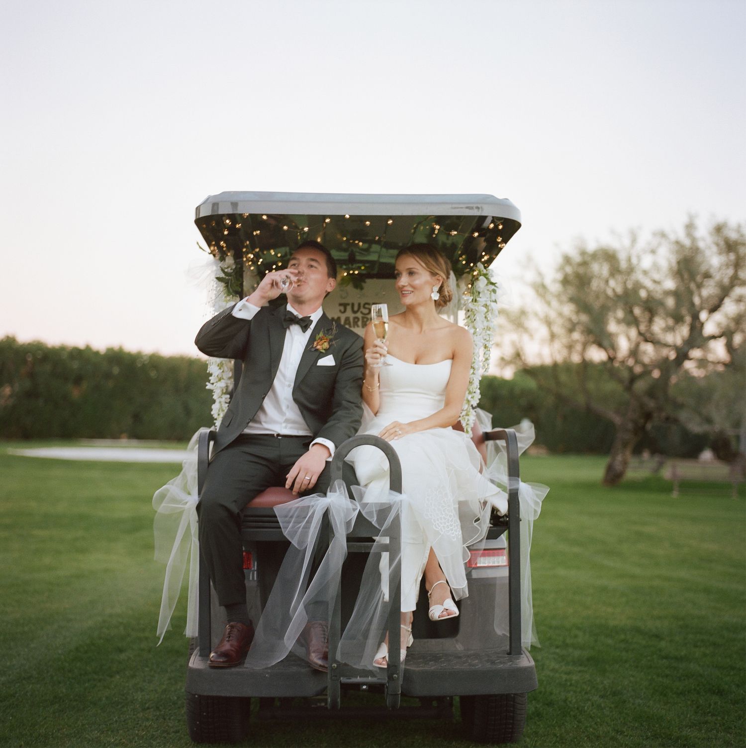 Couple sitting together on a white bench in a garden setting at sunset.