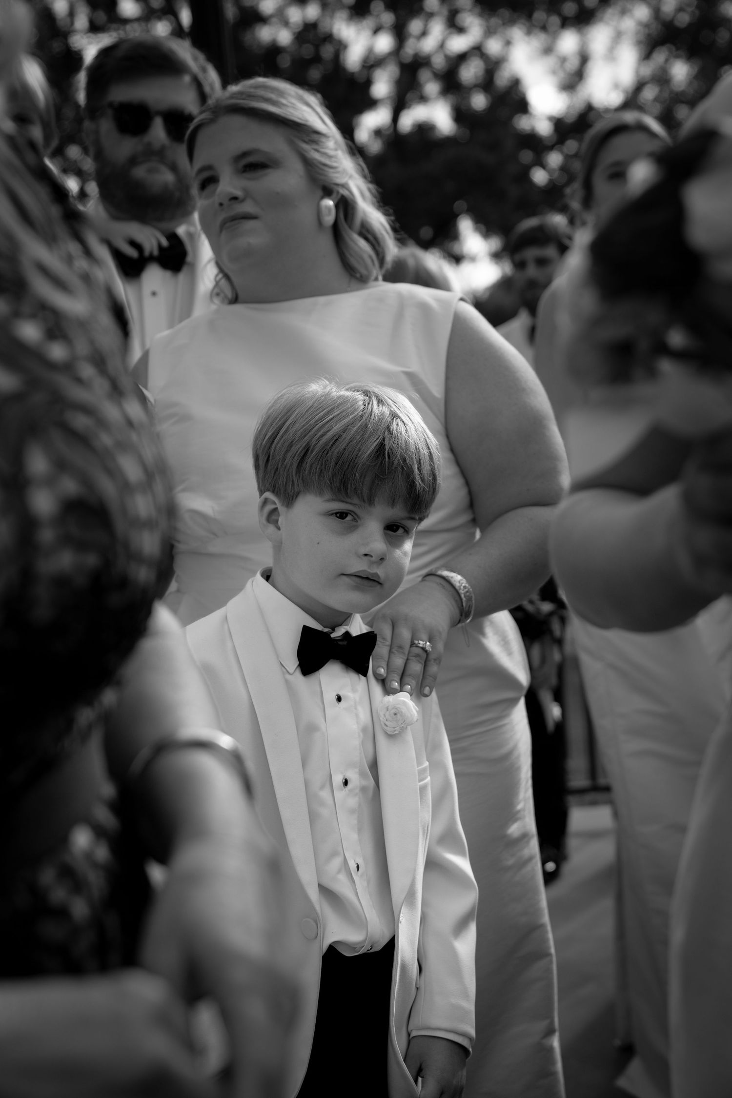 Young ring bearer in formal black tuxedo and bow tie at an elegant wedding ceremony.