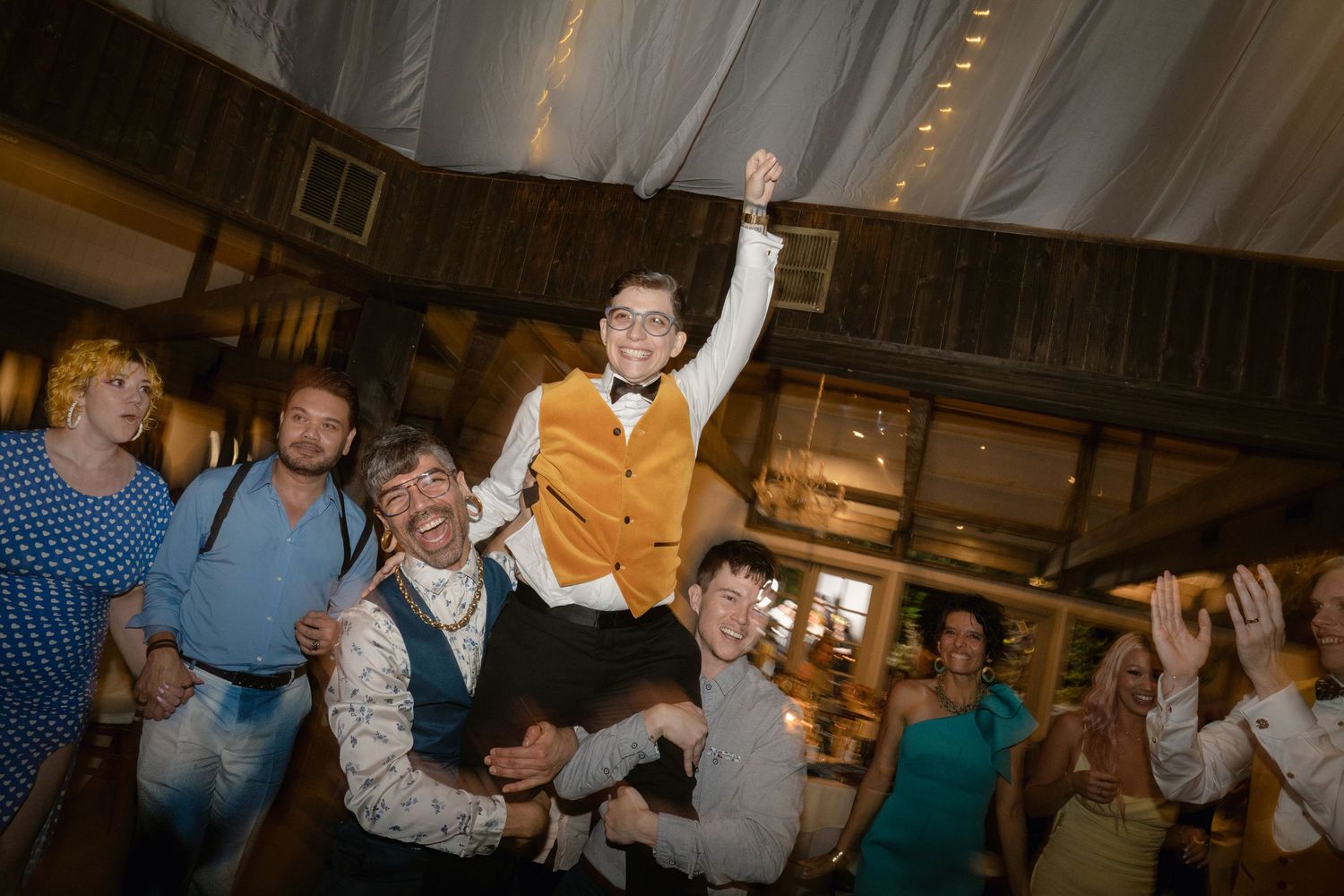 People dancing and celebrating with raised arms at an indoor reception venue.