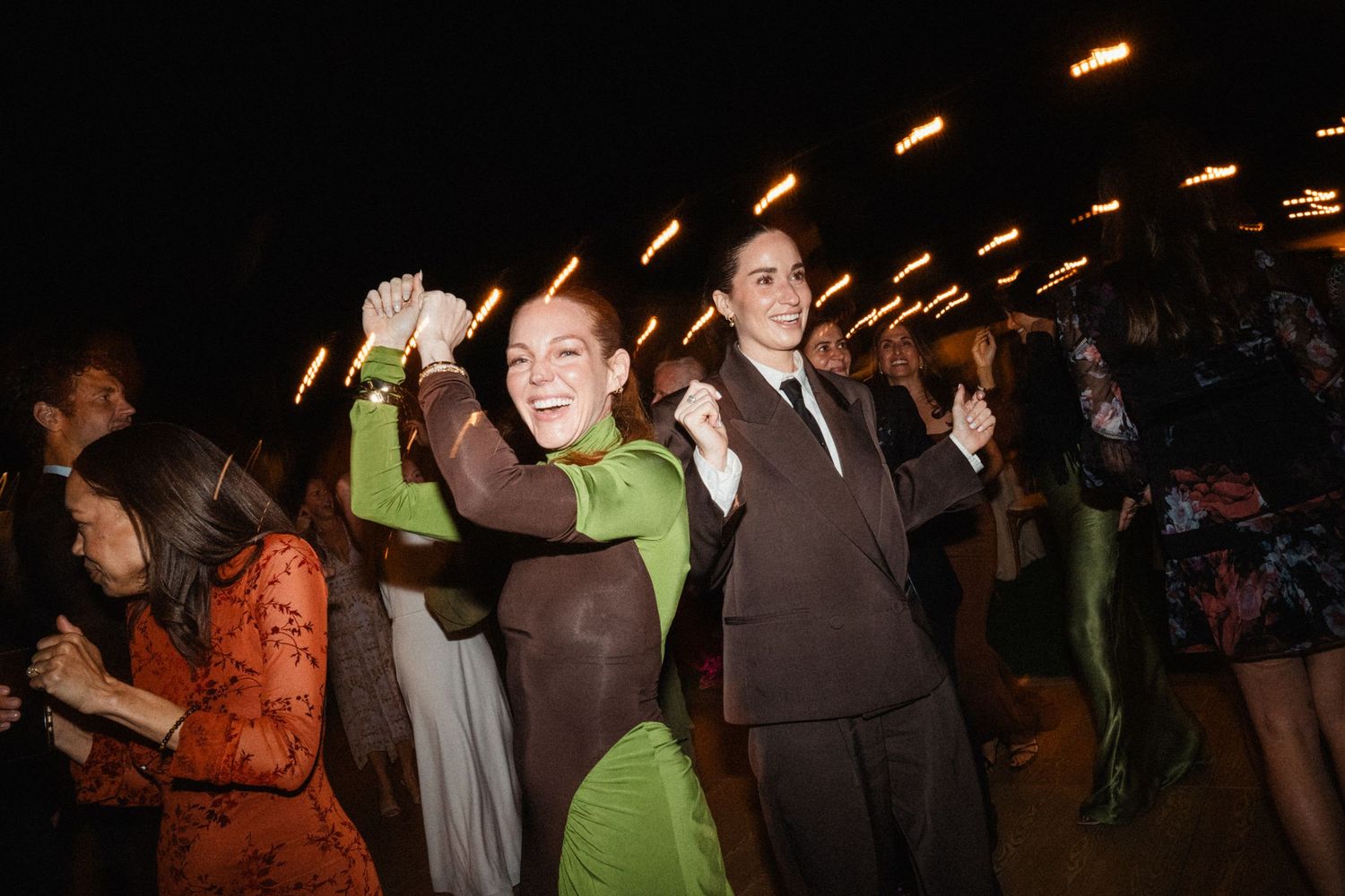 Dark nighttime scene of people mingling at an outdoor party with warm lighting.