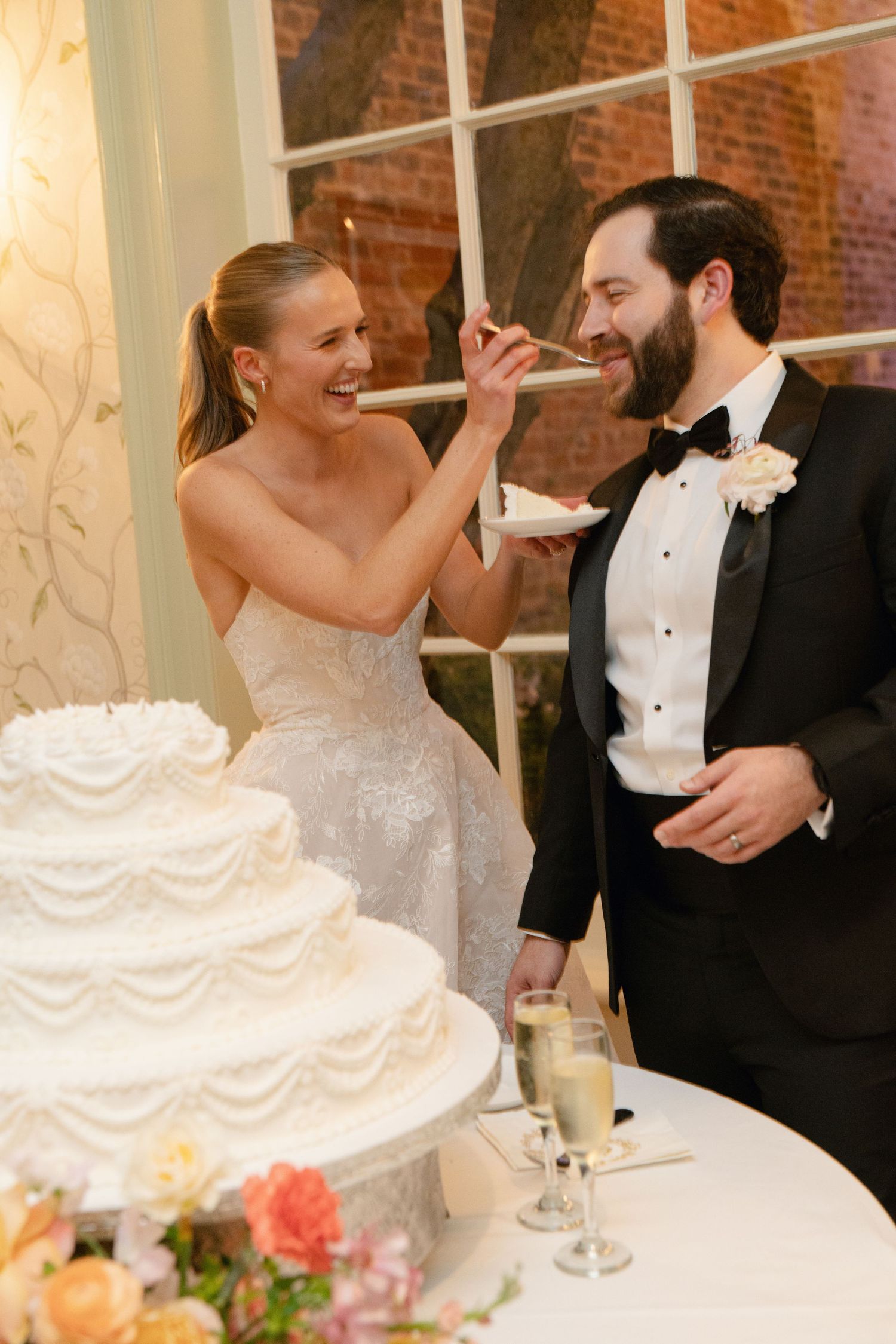 Traditional wedding cake cutting moment with the couple sharing bites of white tiered cake.