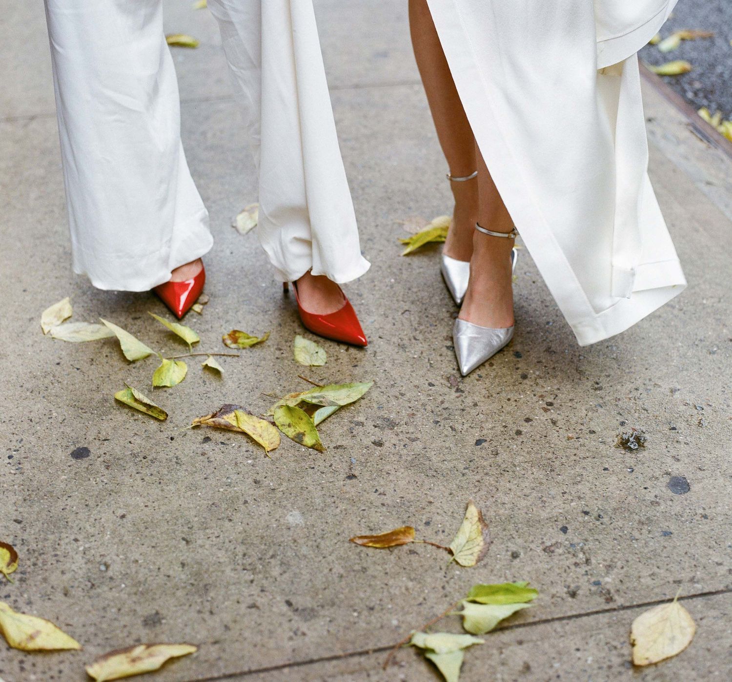 Feet walking on sidewalk with scattered autumn leaves, wearing white formal attire.