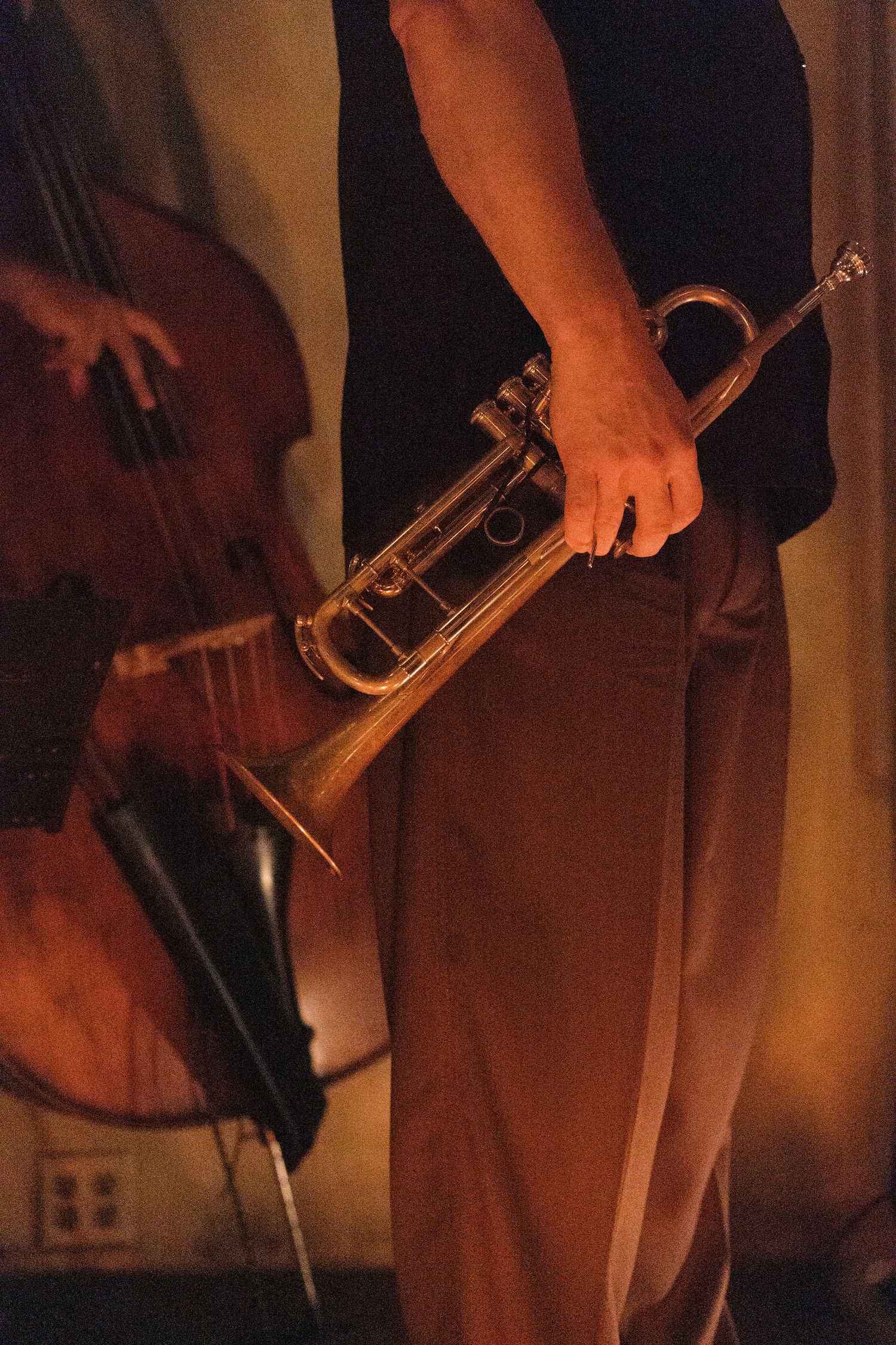 Jazz musician holding a brass trumpet with a double bass player performing in warm amber stage lighting.