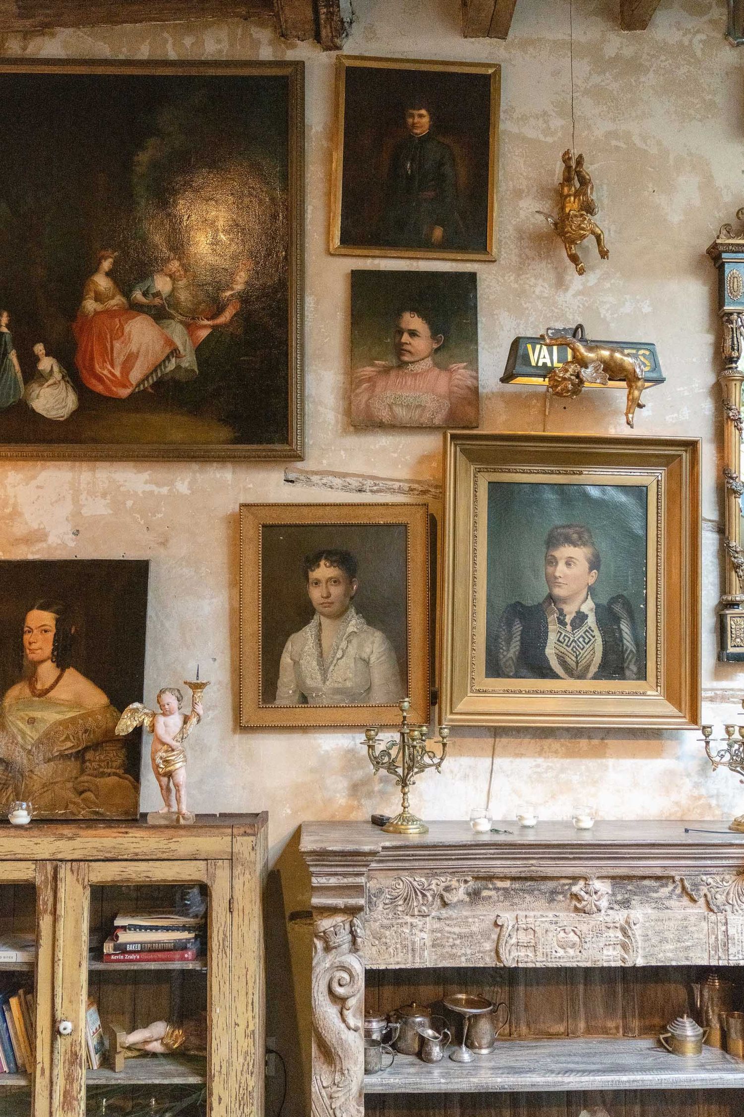 Vintage oil paintings and portraits line the walls of a rustic room with weathered plaster walls.