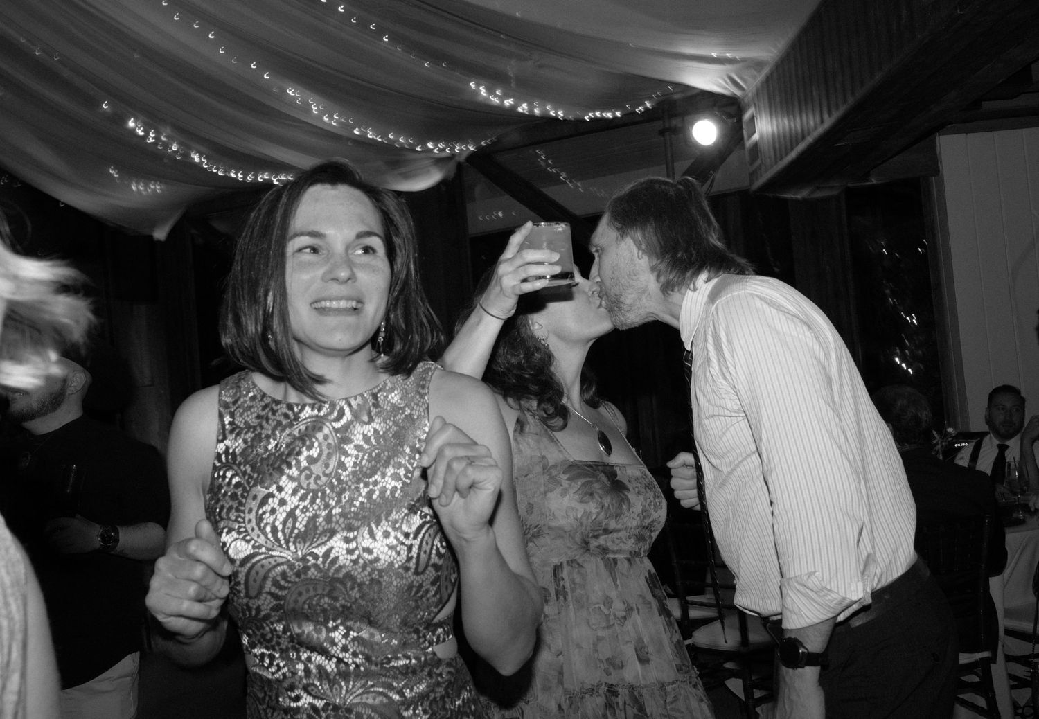 Wedding reception guests dancing under string lights in a tented venue.