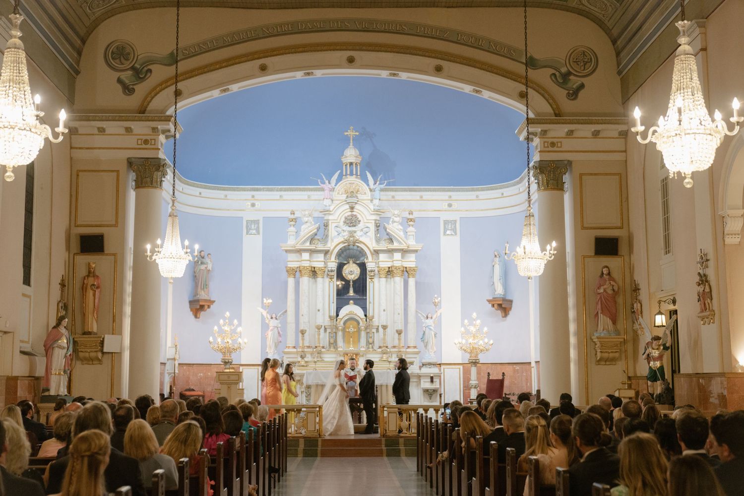 Wide shot of a traditional church interior with white walls and hanging chandeliers.