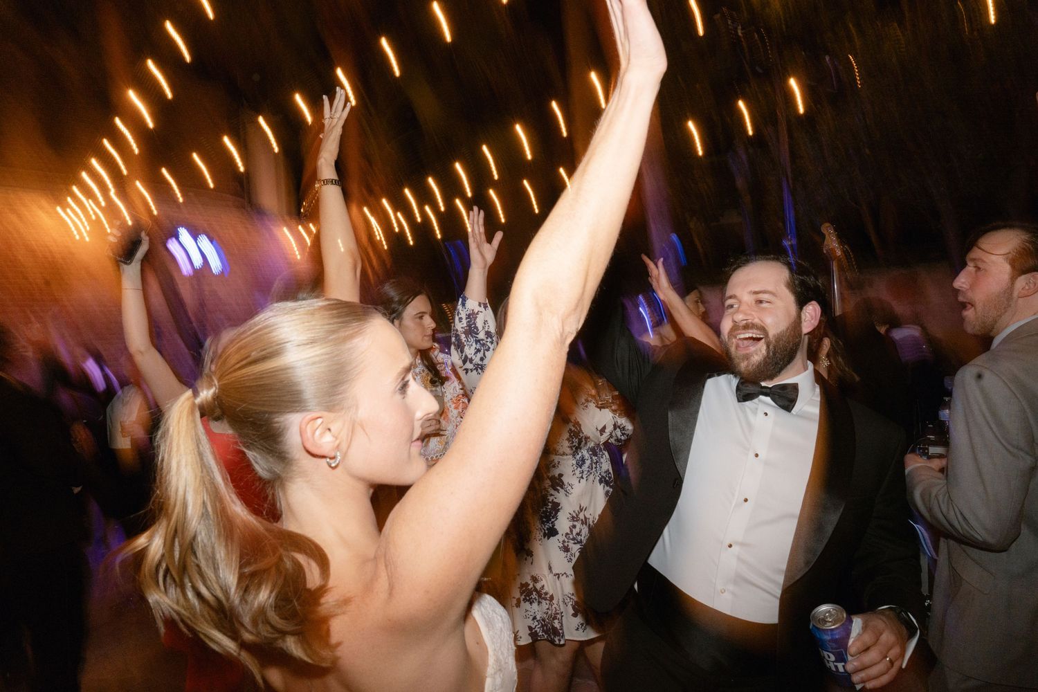 Wedding reception dance party with guests celebrating under warm lighting.