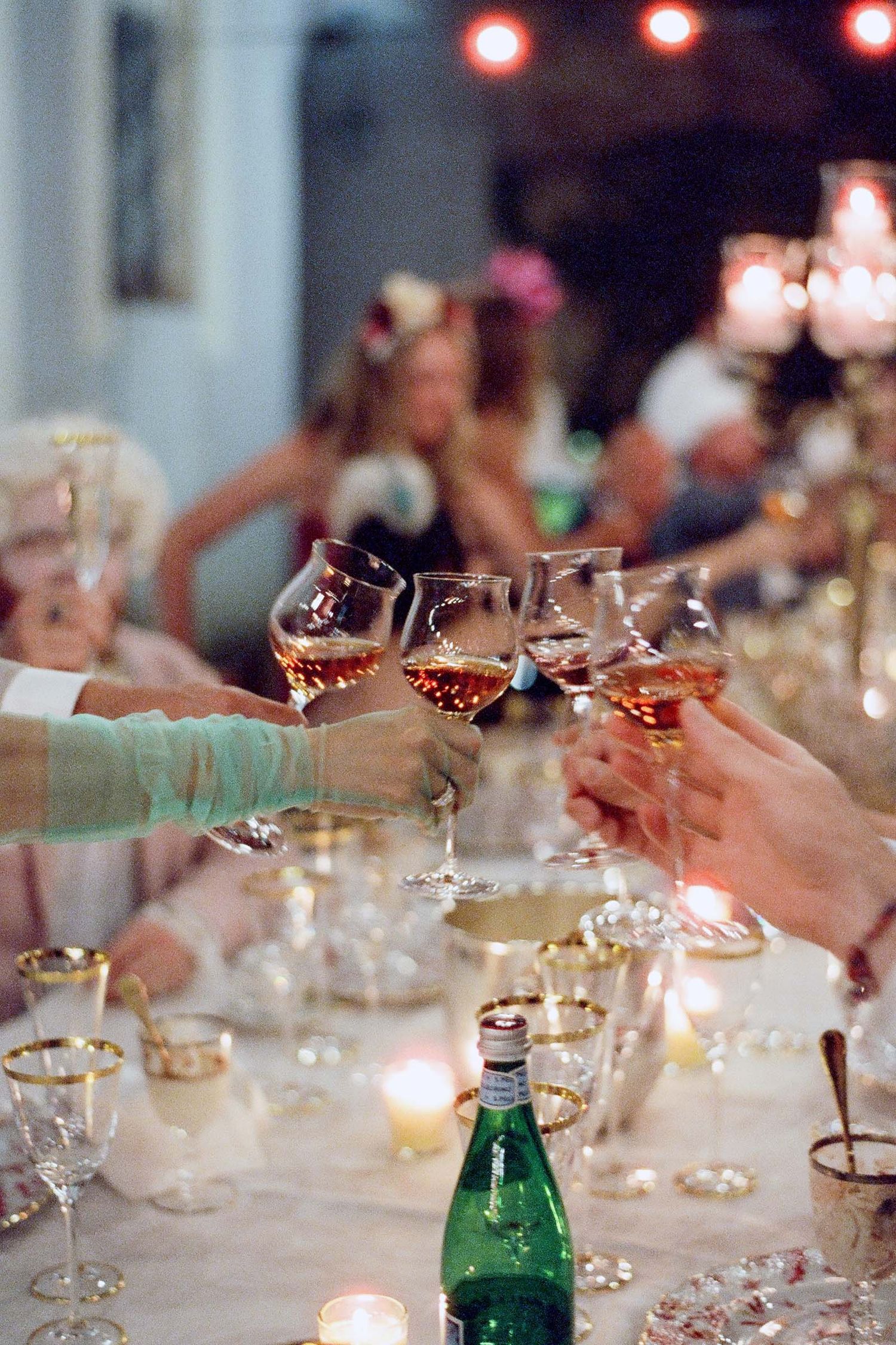 Wine glasses clink together in a celebratory toast across an elegant candlelit dinner table.