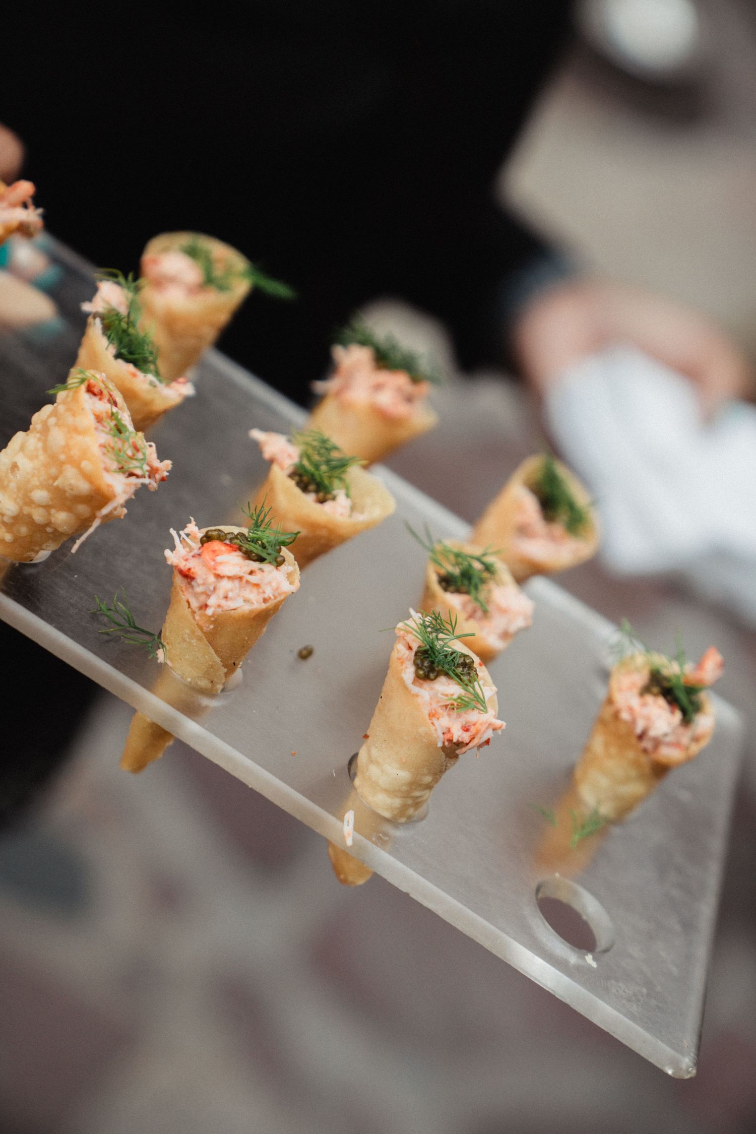 Elegant appetizers served in small cone-shaped vessels on clear display plates.