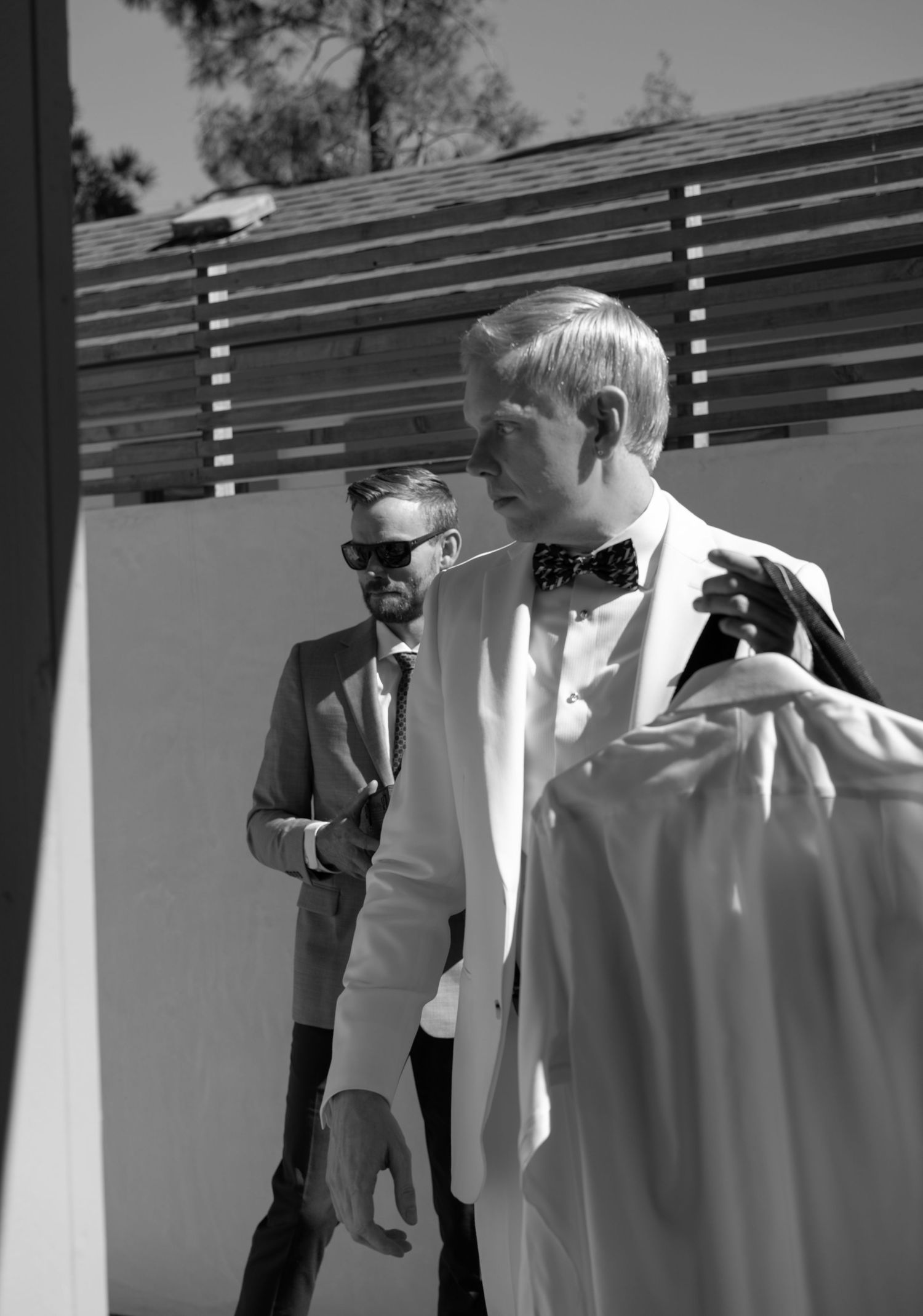 Black and white photo of groomsmen in formal attire standing against a slatted wall.