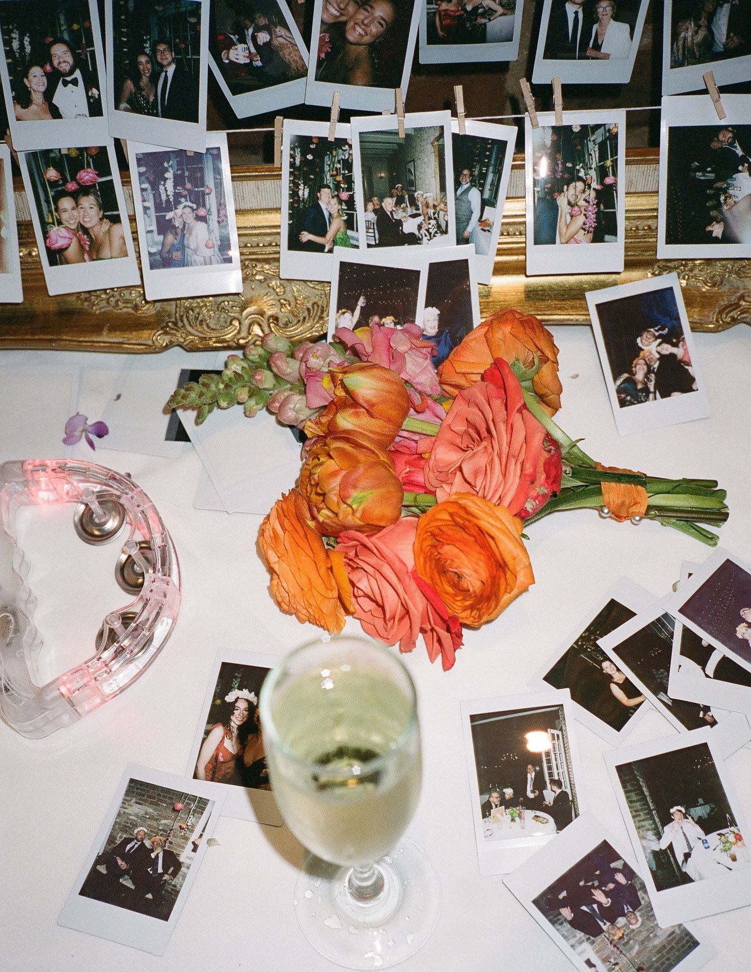 Wedding reception table decorated with orange flowers and polaroid photos displayed on white tablecloth.