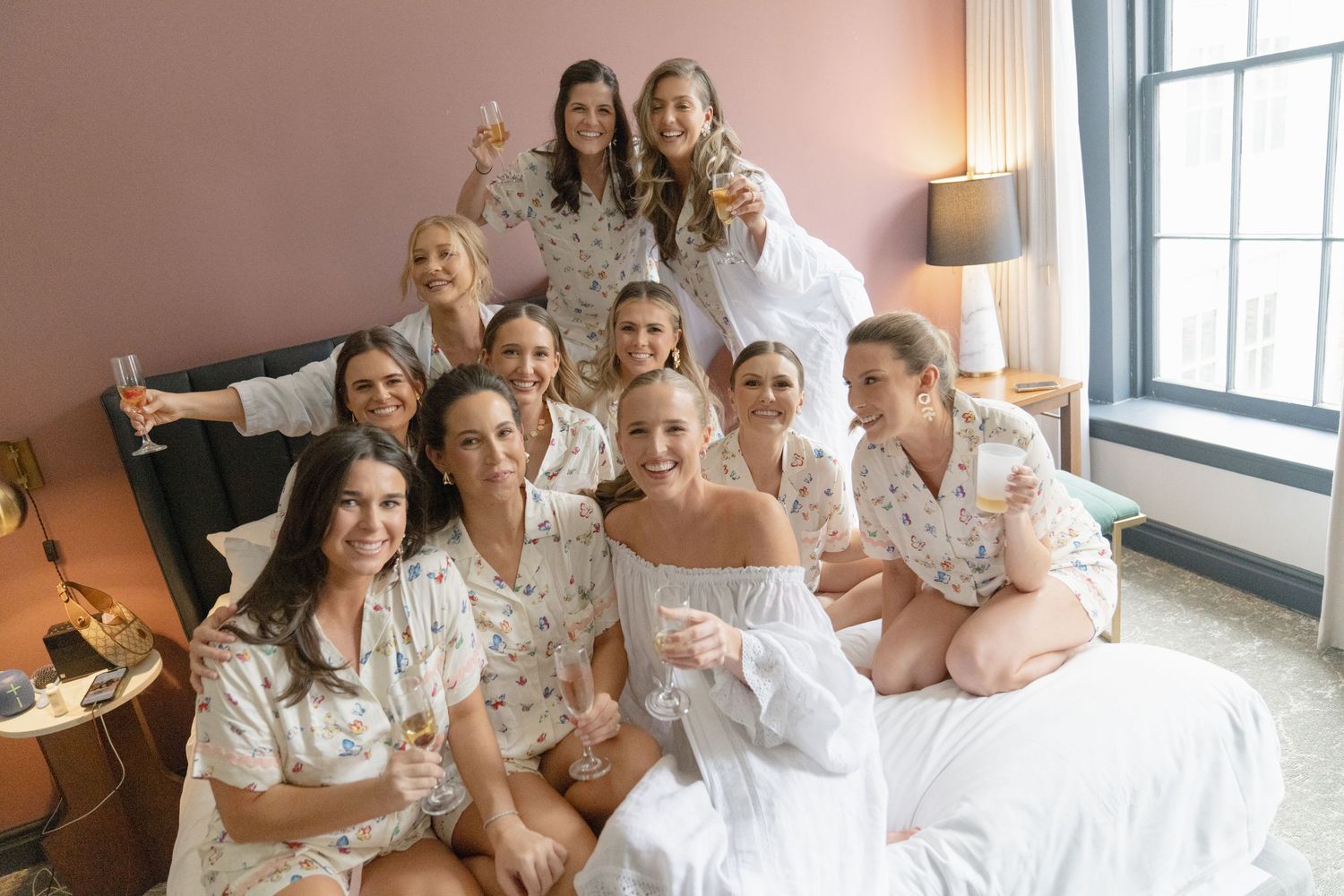 Friends in matching floral robes share champagne and laughter during wedding morning festivities.