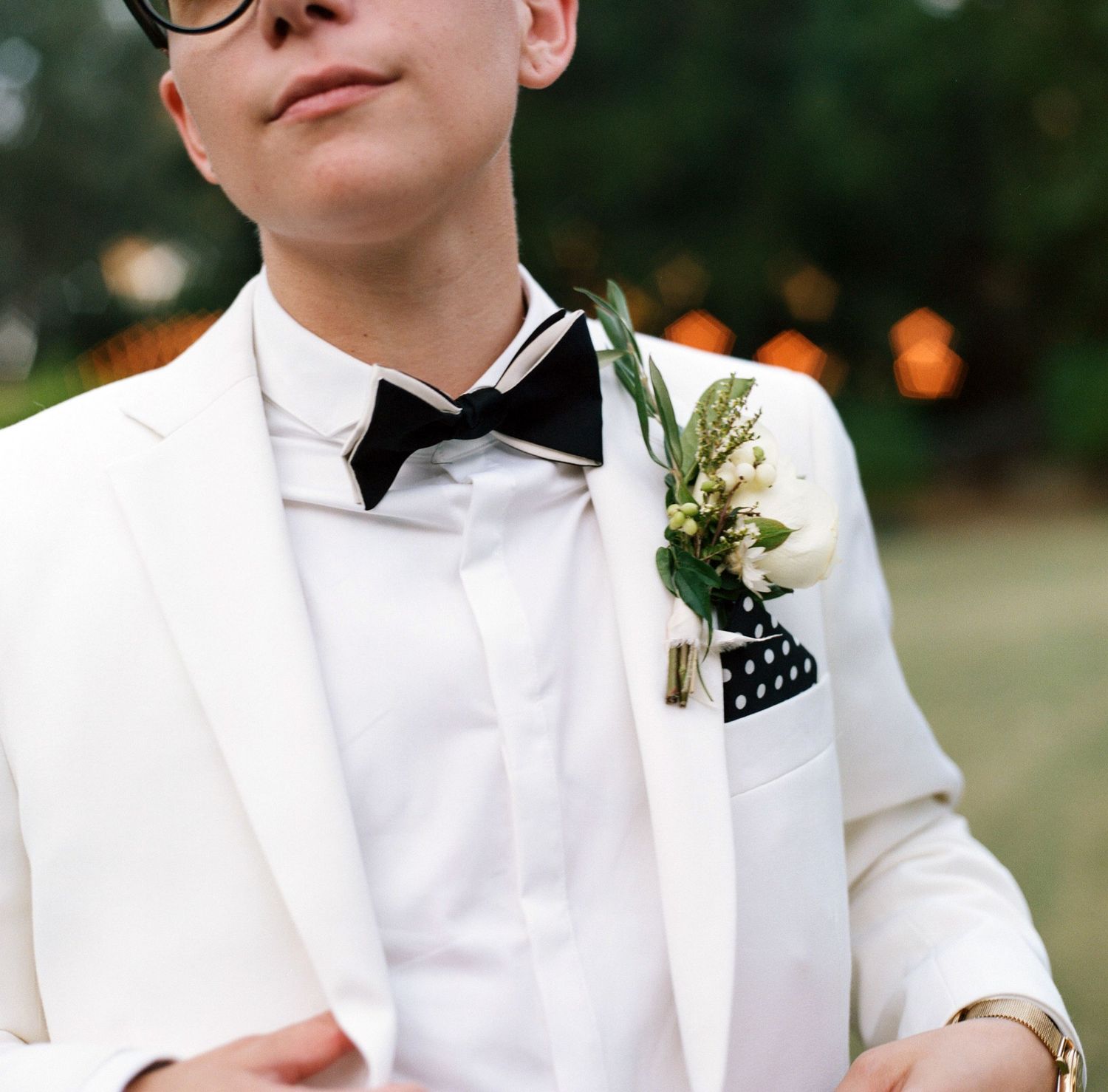 Close-up details of formal white tuxedo jackets with boutonnieres and bow ties.