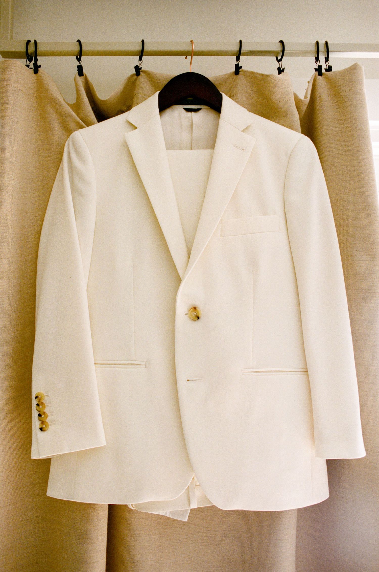 Row of crisp white suit jackets hanging on garment rack against beige background.