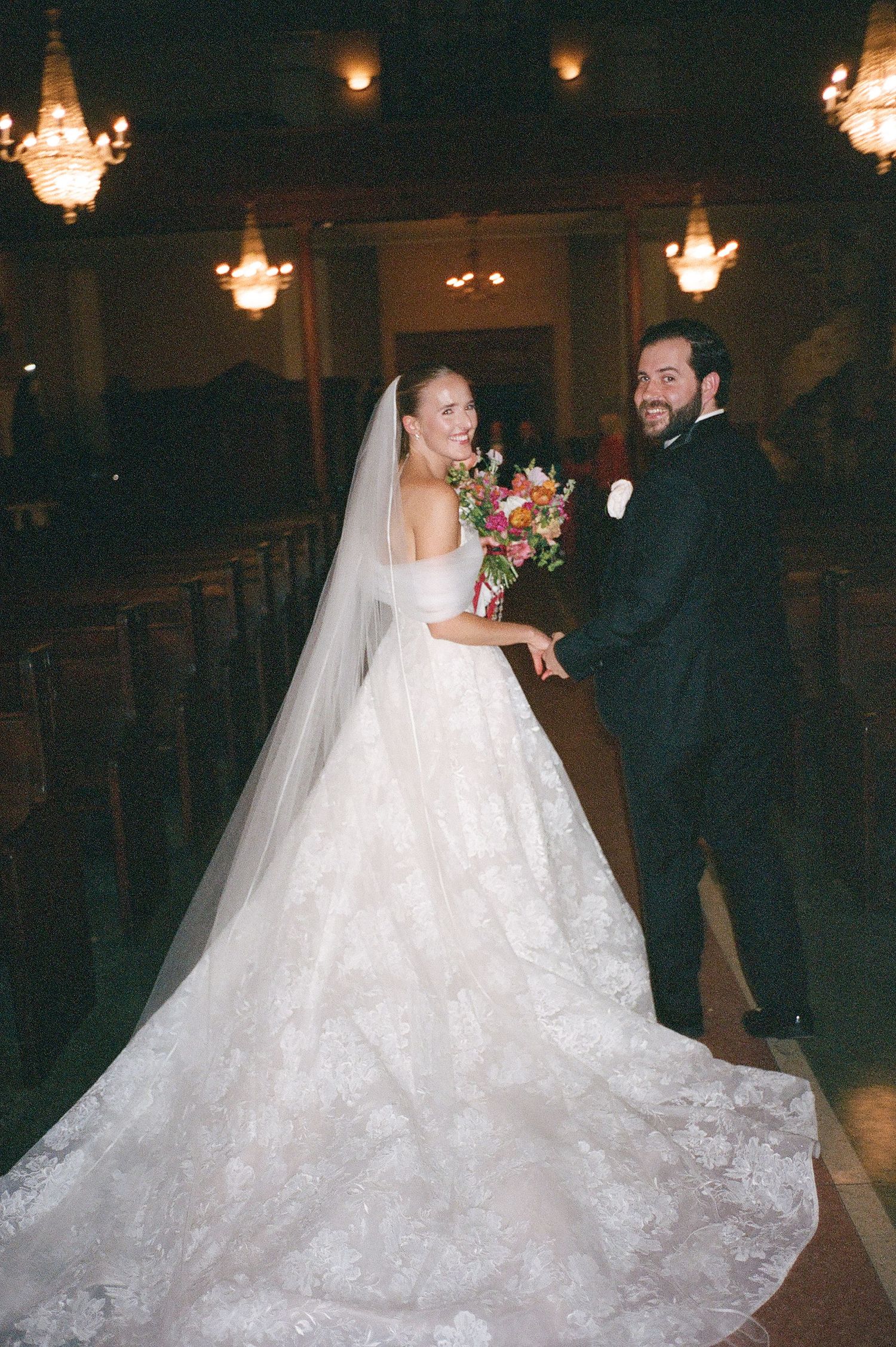 A bride in a flowing white wedding gown with a dramatic train dances with her partner at an elegant reception.