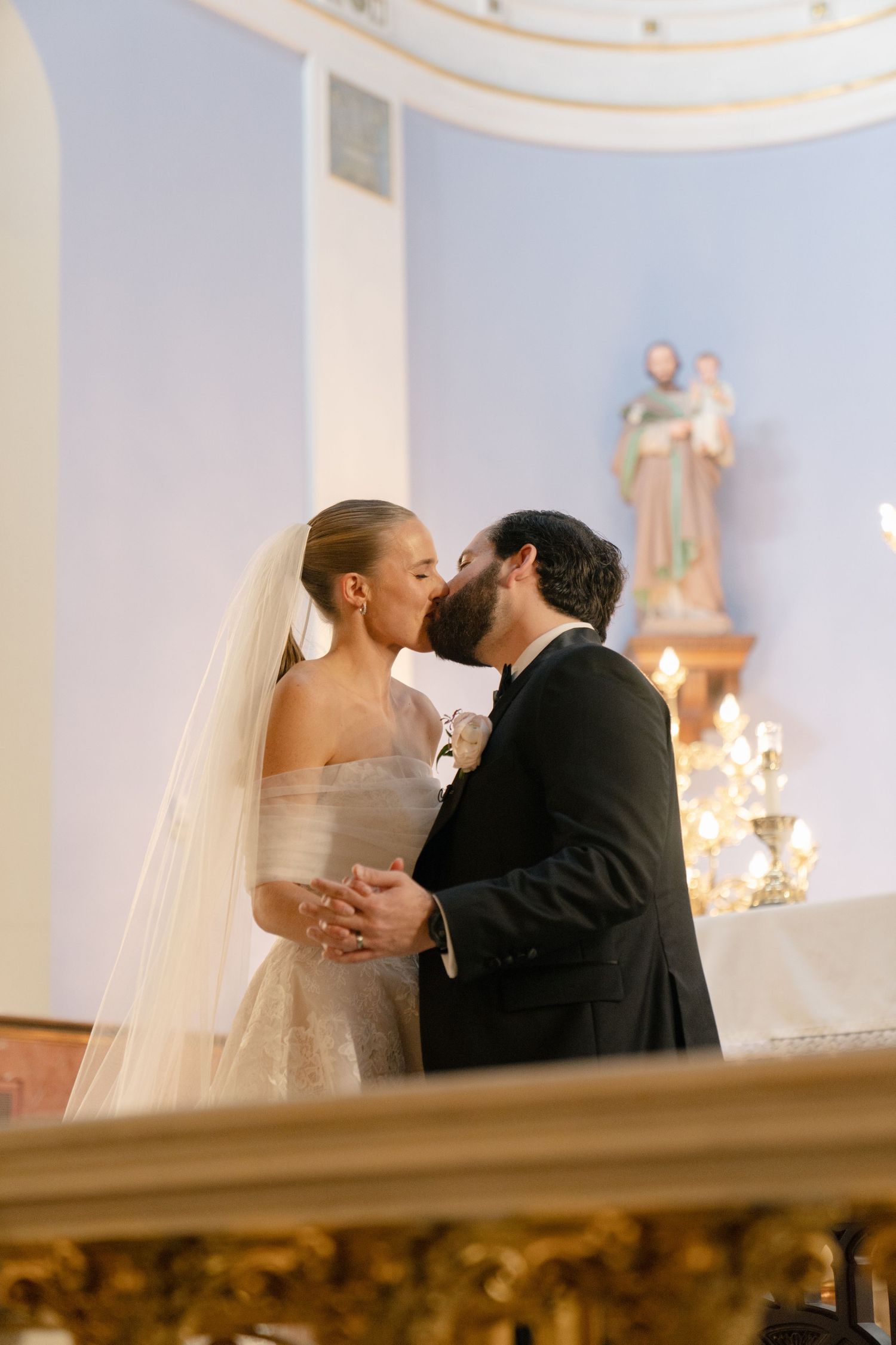 Romantic wedding ceremony moment inside an elegant church with blue walls and chandeliers.